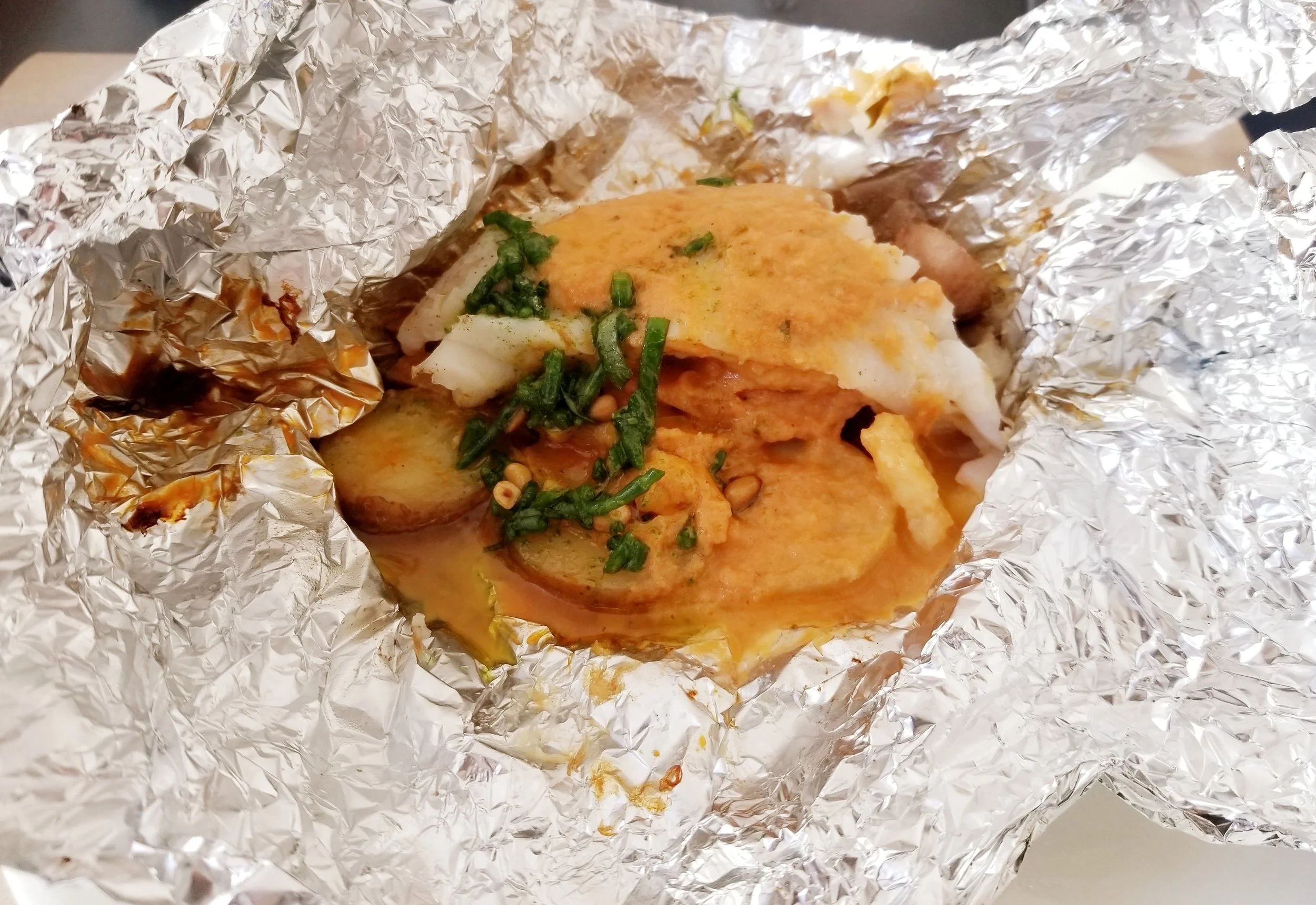 Papillote (package) of Lieu Jaune (Pollock) with potatoes and piperade. For this preparation, the fish is cooked in aluminum foil with its accompaniments.