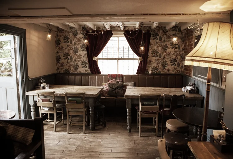 The back dining room with long wooden tables and floral wallpaper