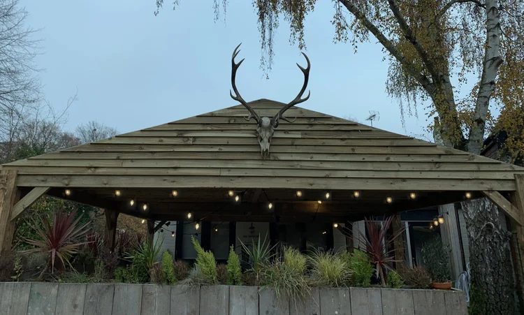 The Stable, a covered timber shelter with festoon lights and a stag's head