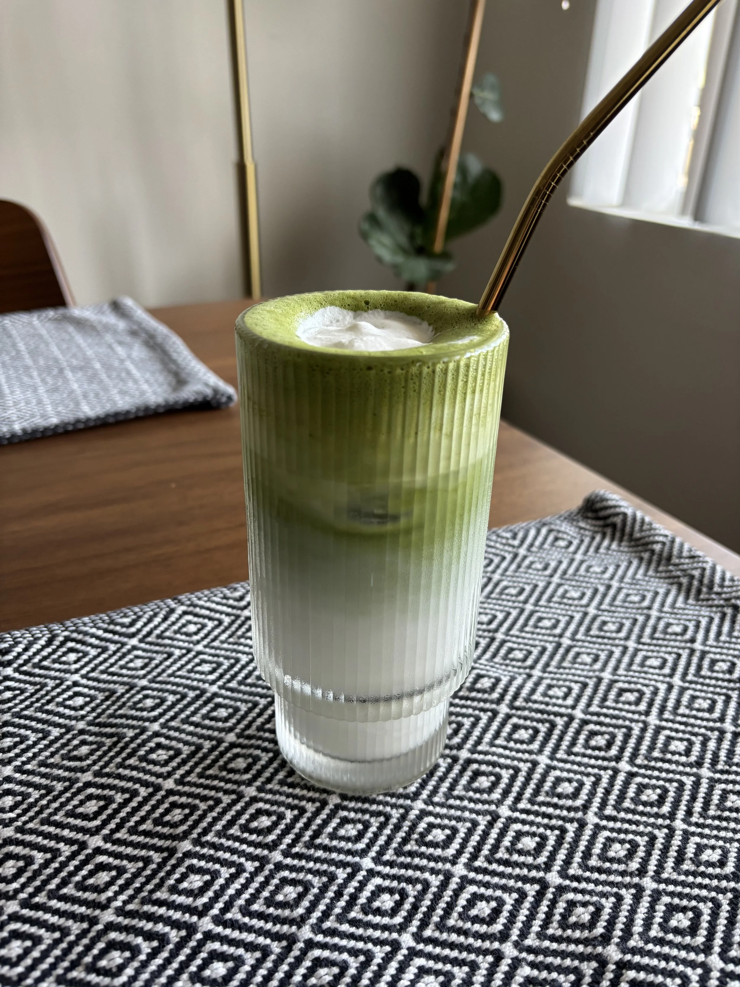 A glass of iced matcha latte with an ombre swirl of green matcha on top and white milk on the bottom.