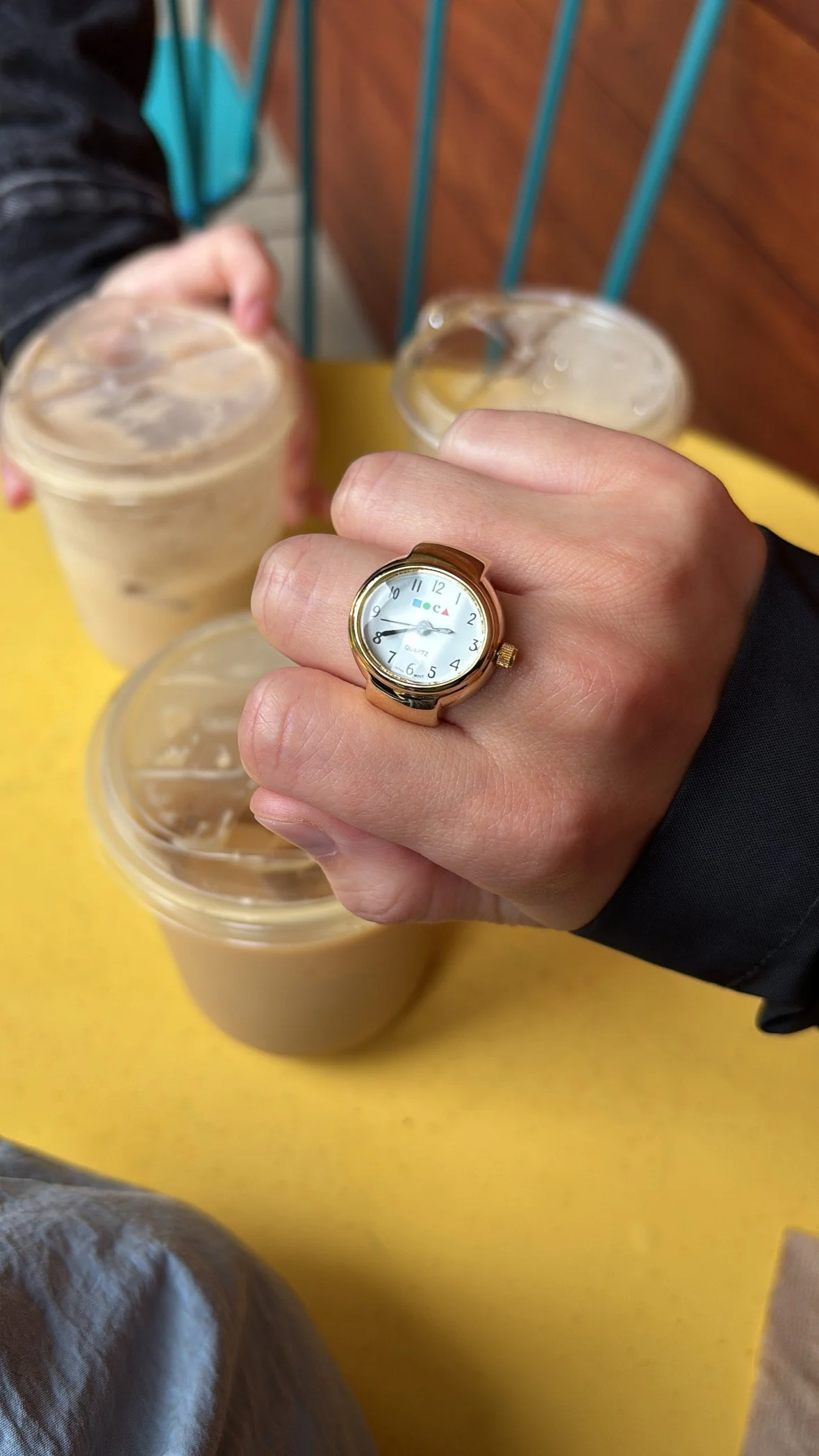 A closed hand with a gold ring of a mini watch with the logo of the Museum of Contemporary Art inside.