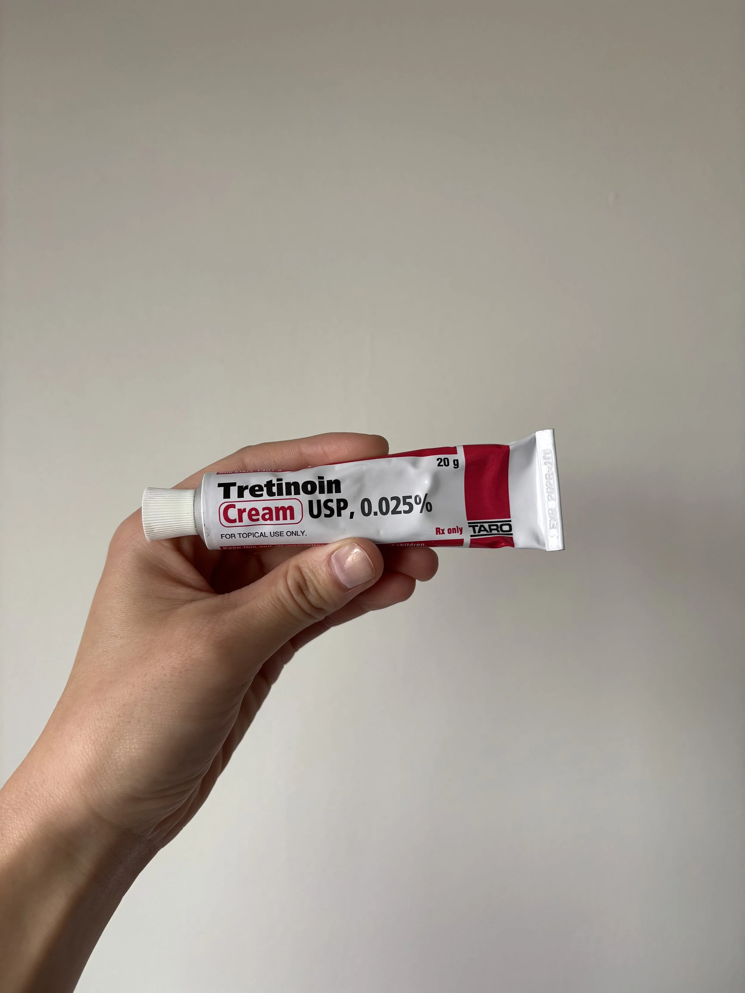 Hand holding up a small, slender Trentinoin cream bottle with 0.025% written on it