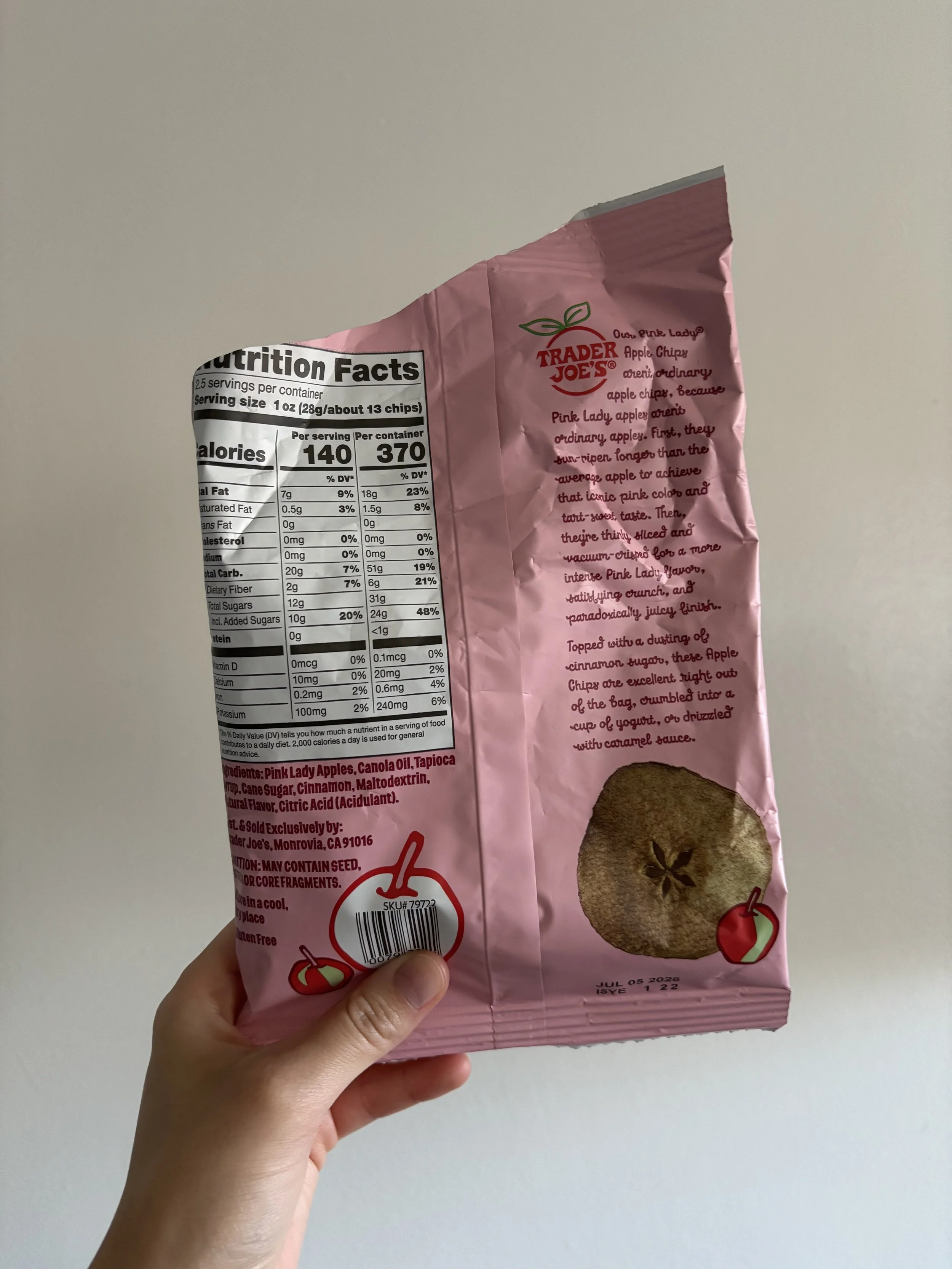 A woman's hand holding the bottom left corner of the Trader Joe's Pink Lady apple chips