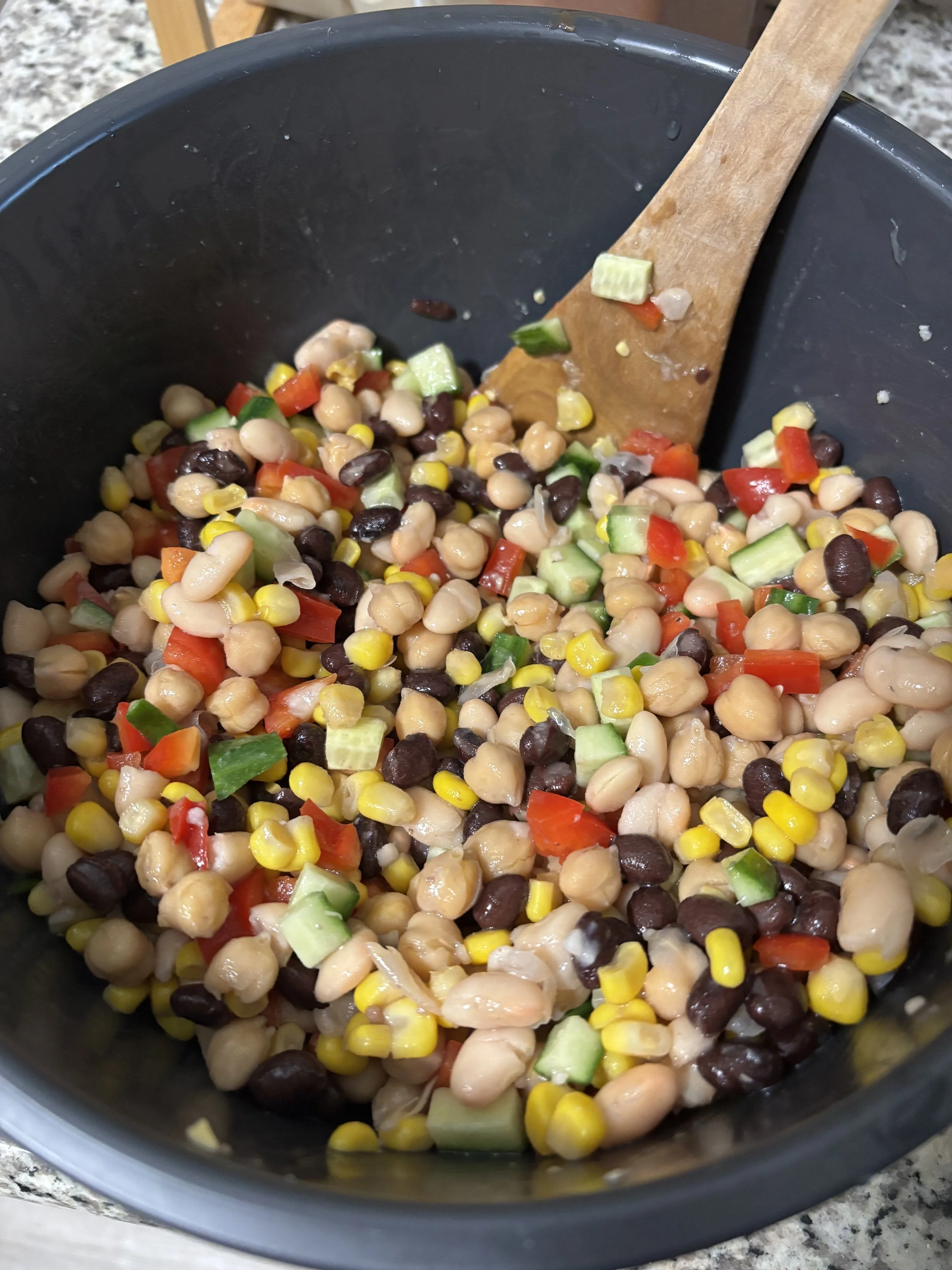 Bowl of bean salad with ingredients such as chickpeas, cucumbers, black beans, and corn present.