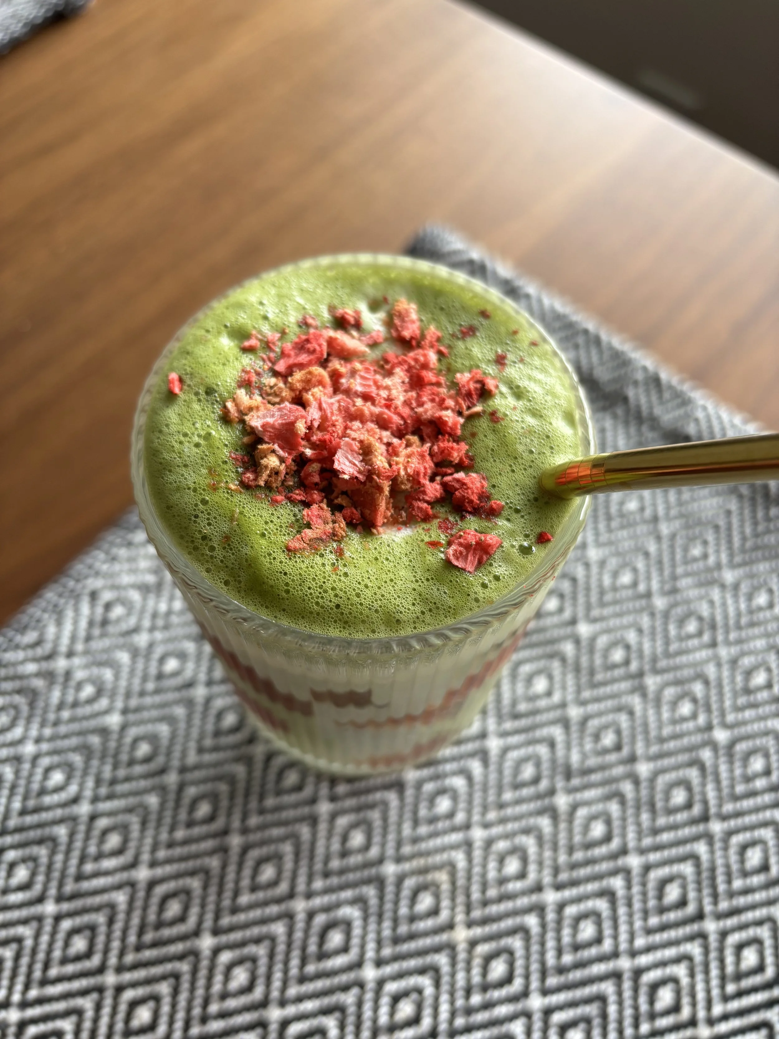 A shot of the same matcha latte drink, but at the top angle with a zoom in on the crushed dried starwberry bits.