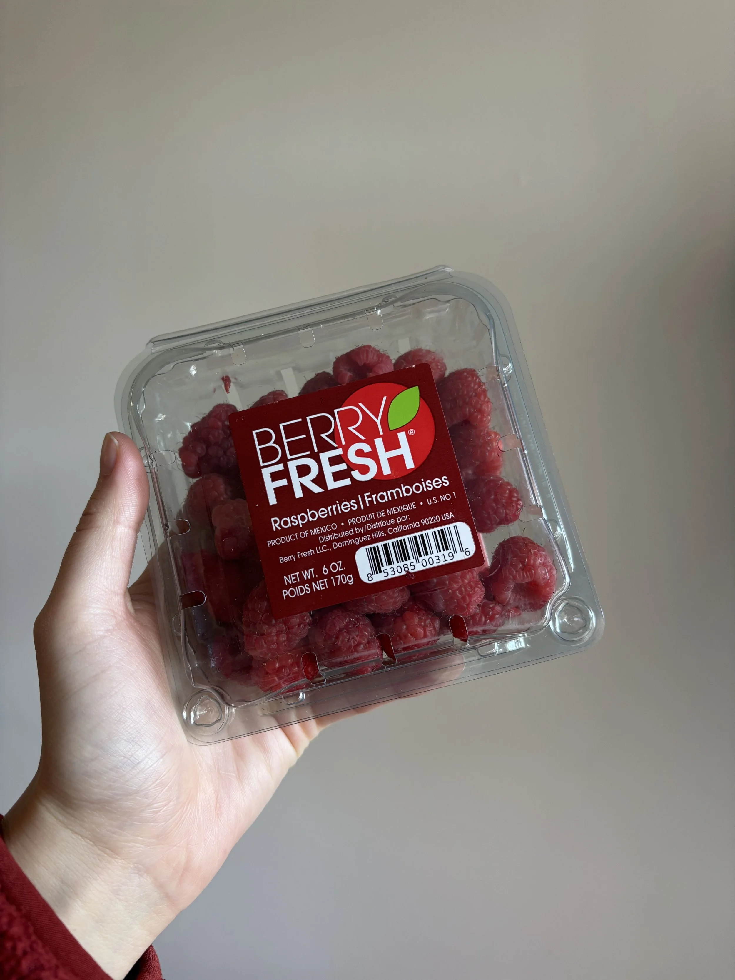 Hand holding up a clear plastic container of raspberries