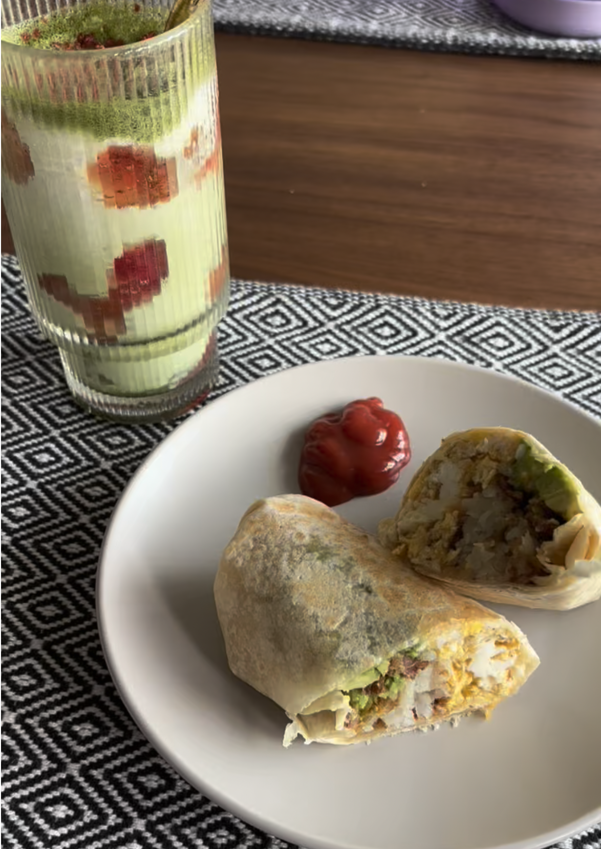 Photo of a burrito cut in half on a plate with an iced matcha latte, all on a patterned placemat.