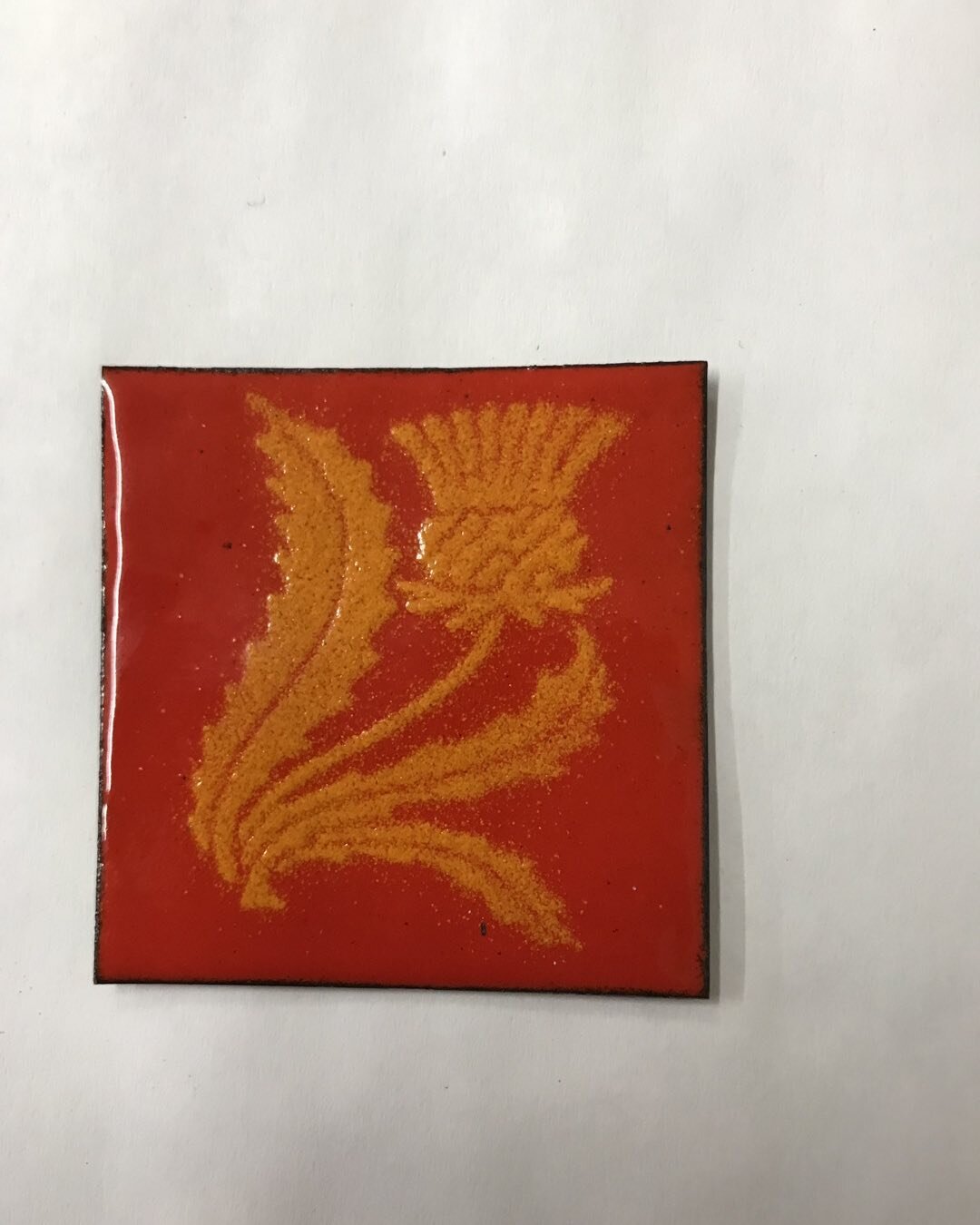 Now on to enameling! Week long class began today at John C Campbell Folk School.  This is my first little piece.  I love the flame orange red background.  The thistle was &ldquo;orange peel&rdquo; firing&hellip;a bit cooler and shorter so it is a bit