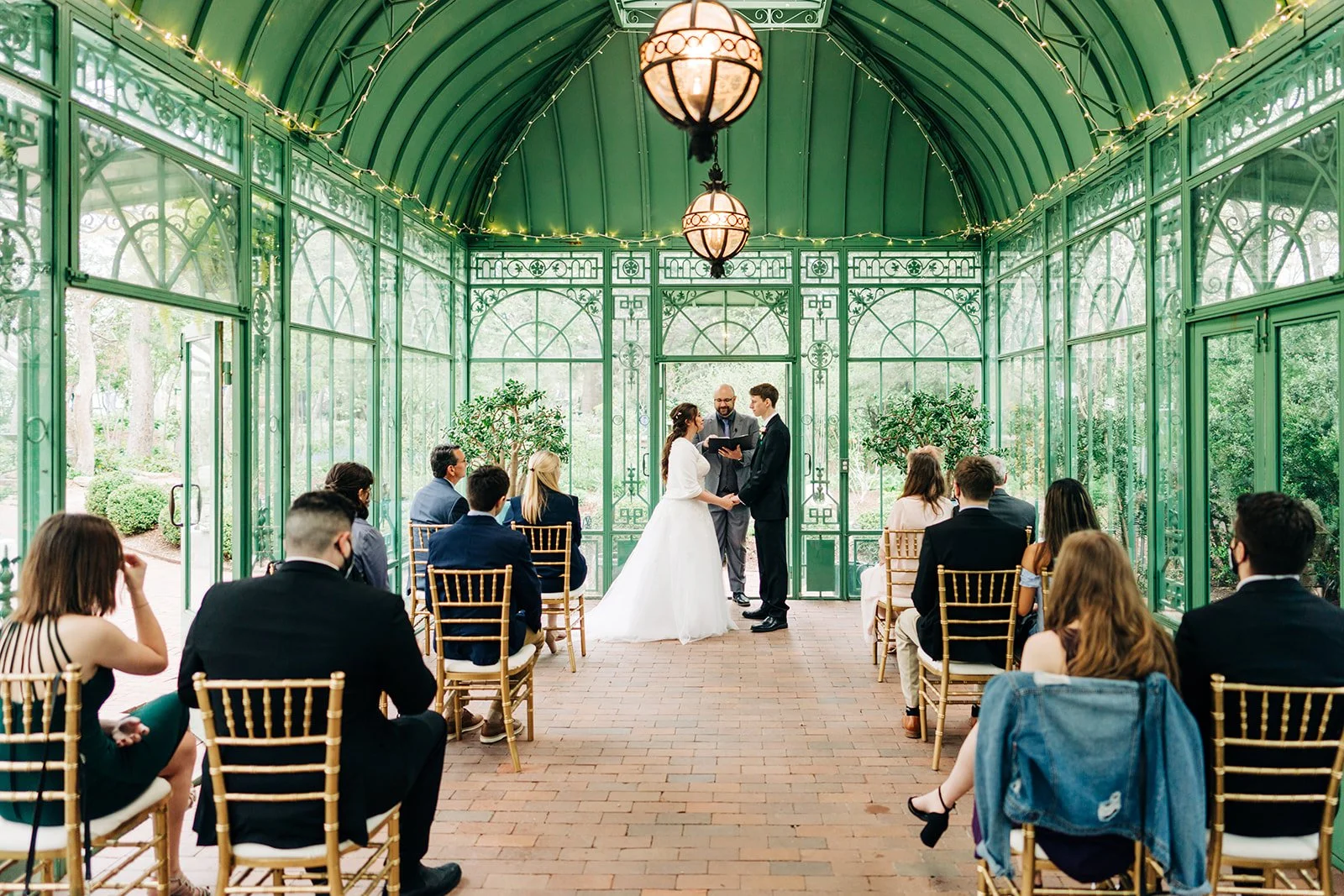 beautiful wedding in the woodland mosaic in denver botanic gardens, the light comes through the greenhouse windows while the guests watch the wedding ceremony