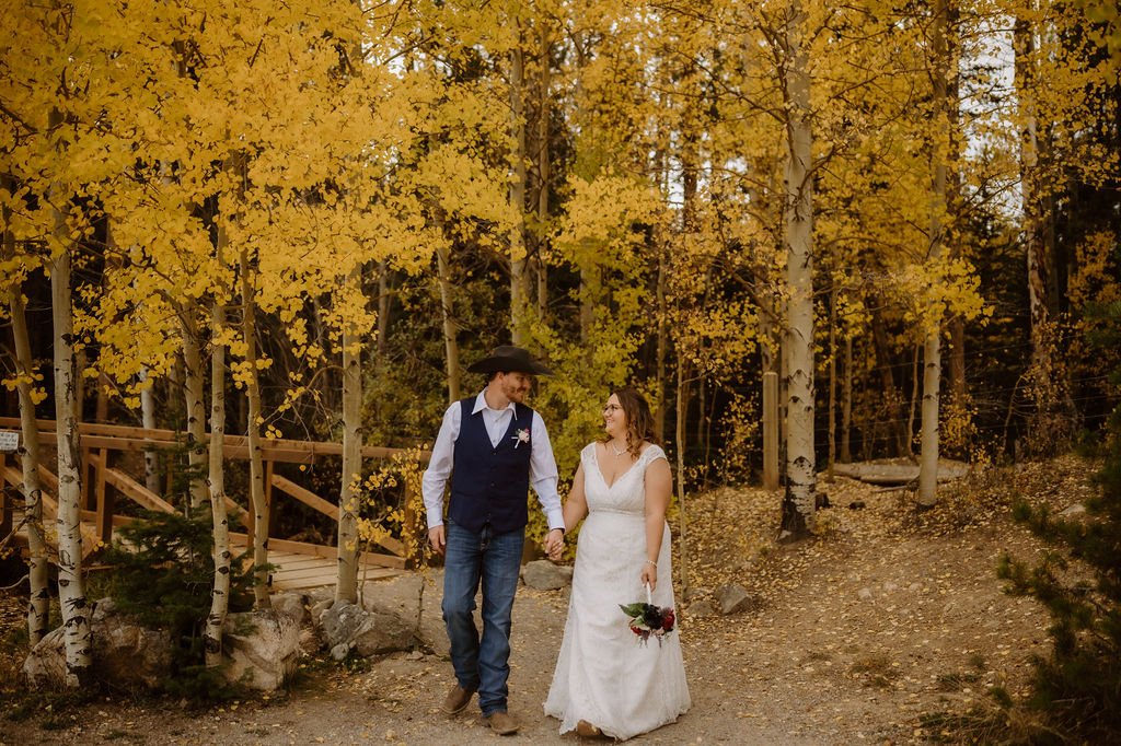 bride and groom walking with yellow aspen trees behind them at sawmill reservoir