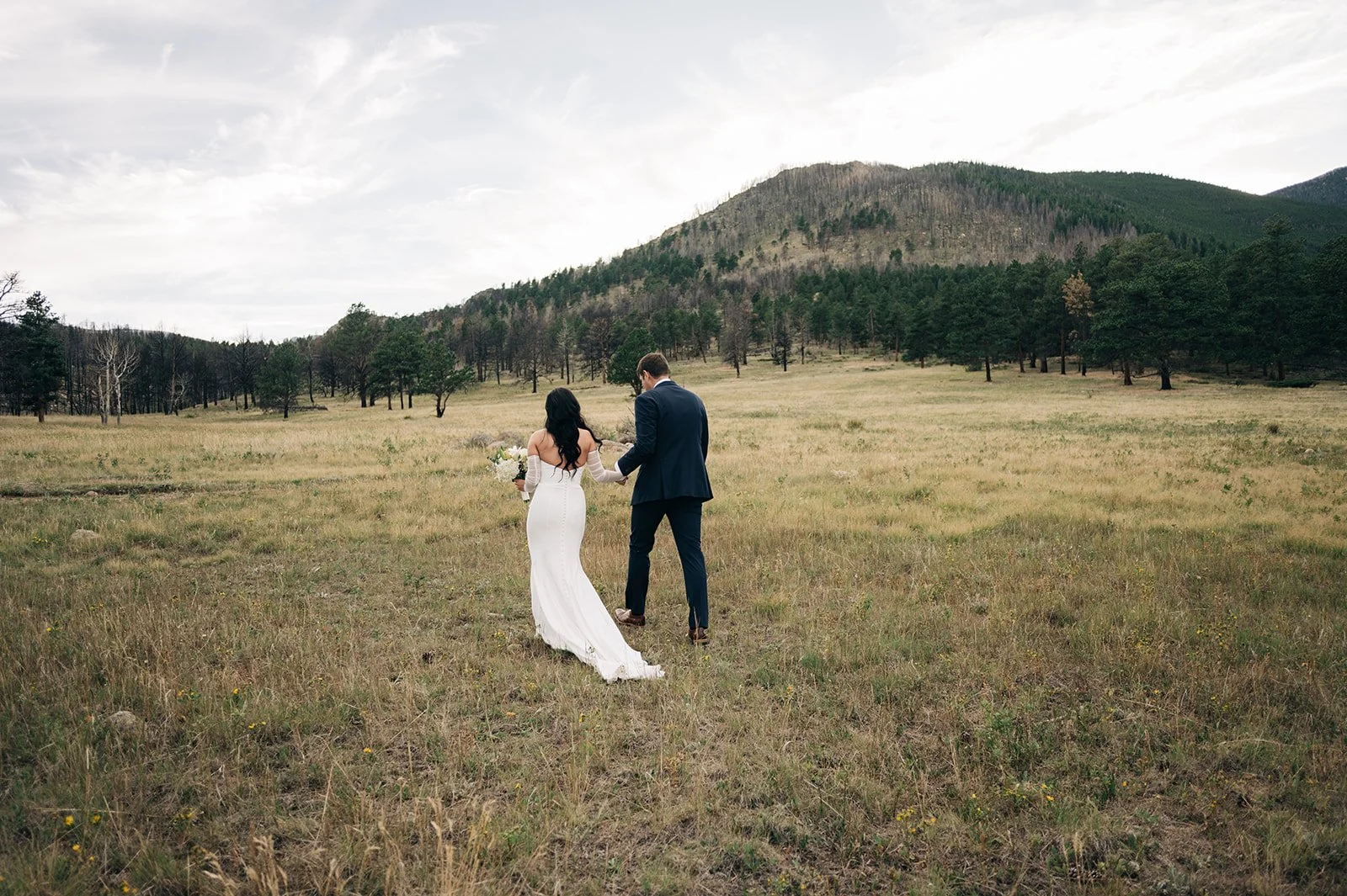 rocky mountain national park upper beaver meadows wedding ceremony site with bride and groom walking in the open field at sunset on a cloudy day