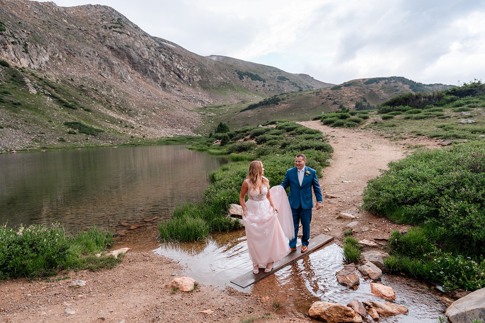 small wedding at loveland pass, near pass lake with bride and groom stepping over a stream.