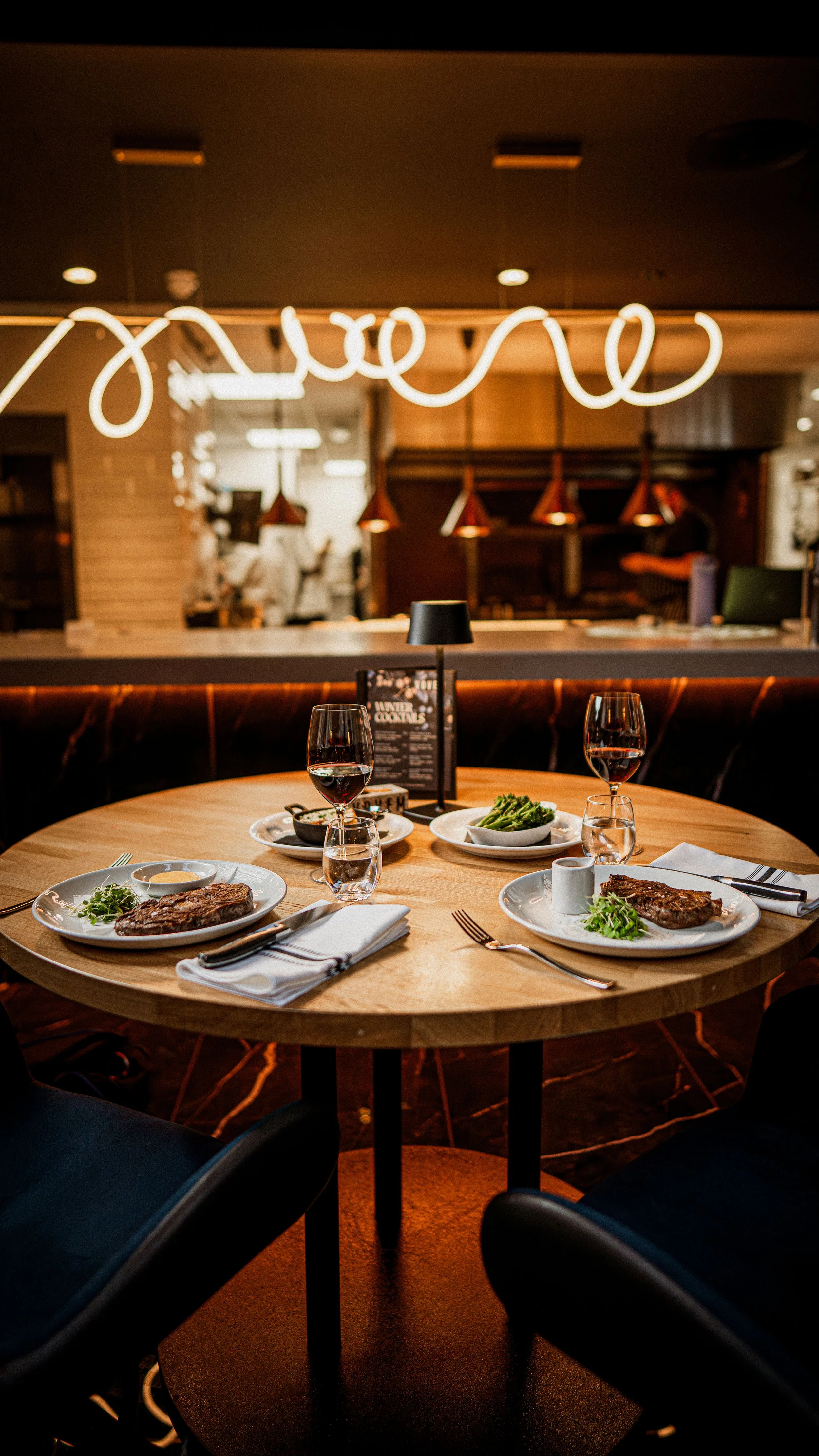 Image of Vovem round table set for the Steak Deal for Two offer, with two steaks and two sides, at a table that views the Ox Grill and kitchen.