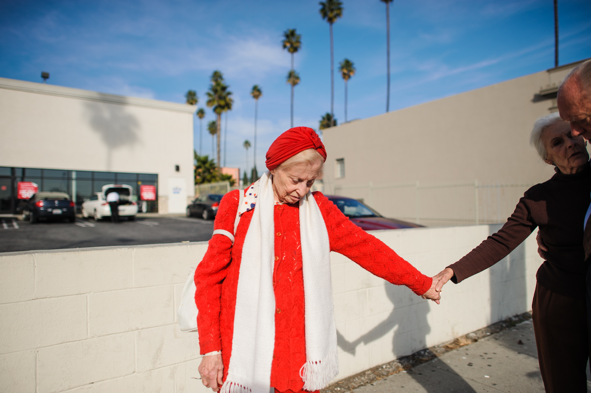  Adina stands on the sidewalk in Los Angeles, as Jeanie holds Adina’s hand while having a conversation with Will.  