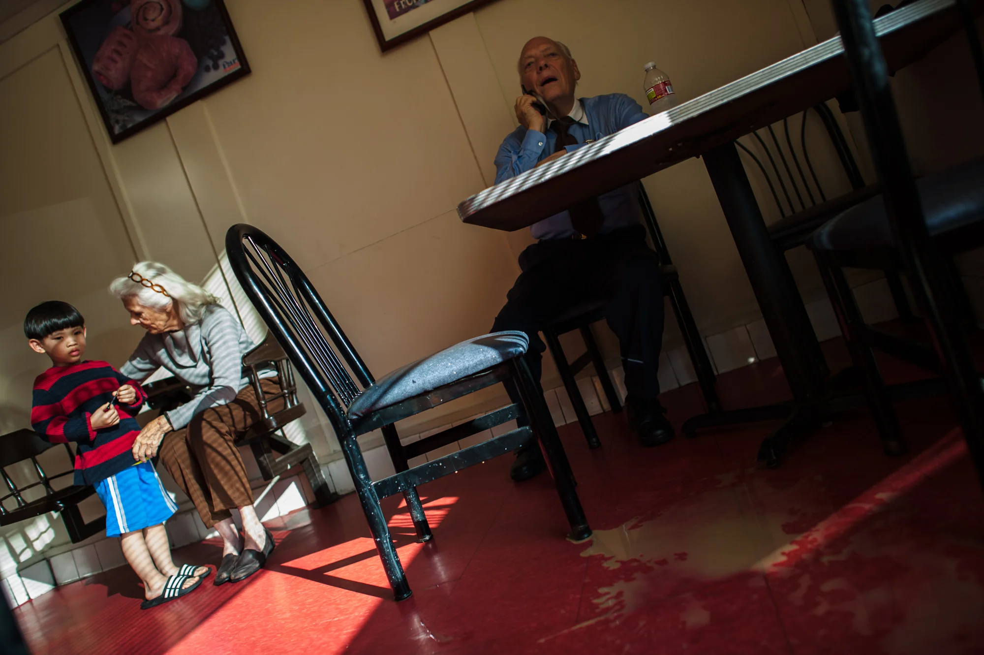 Will speaks on his cell phone, as Jeanie interacts with the donut shop owner’s son who looks at a floor covered in spilled coffee.
