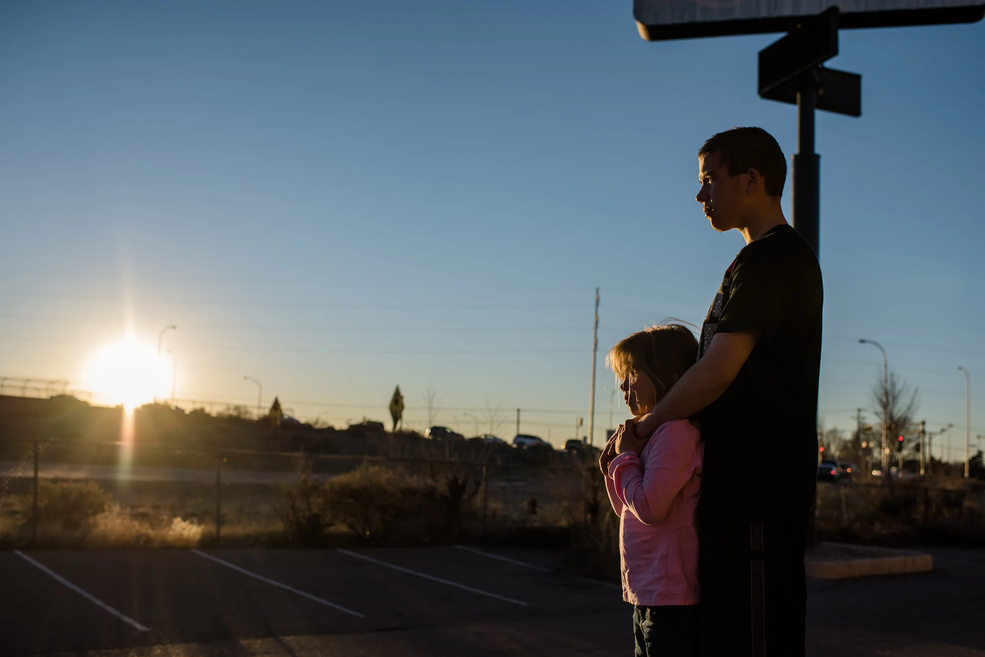 Vinny, age 16, and Elycia, age 7, watch the sunset behind Interstate 40 from the motel parking lot, 2015.
