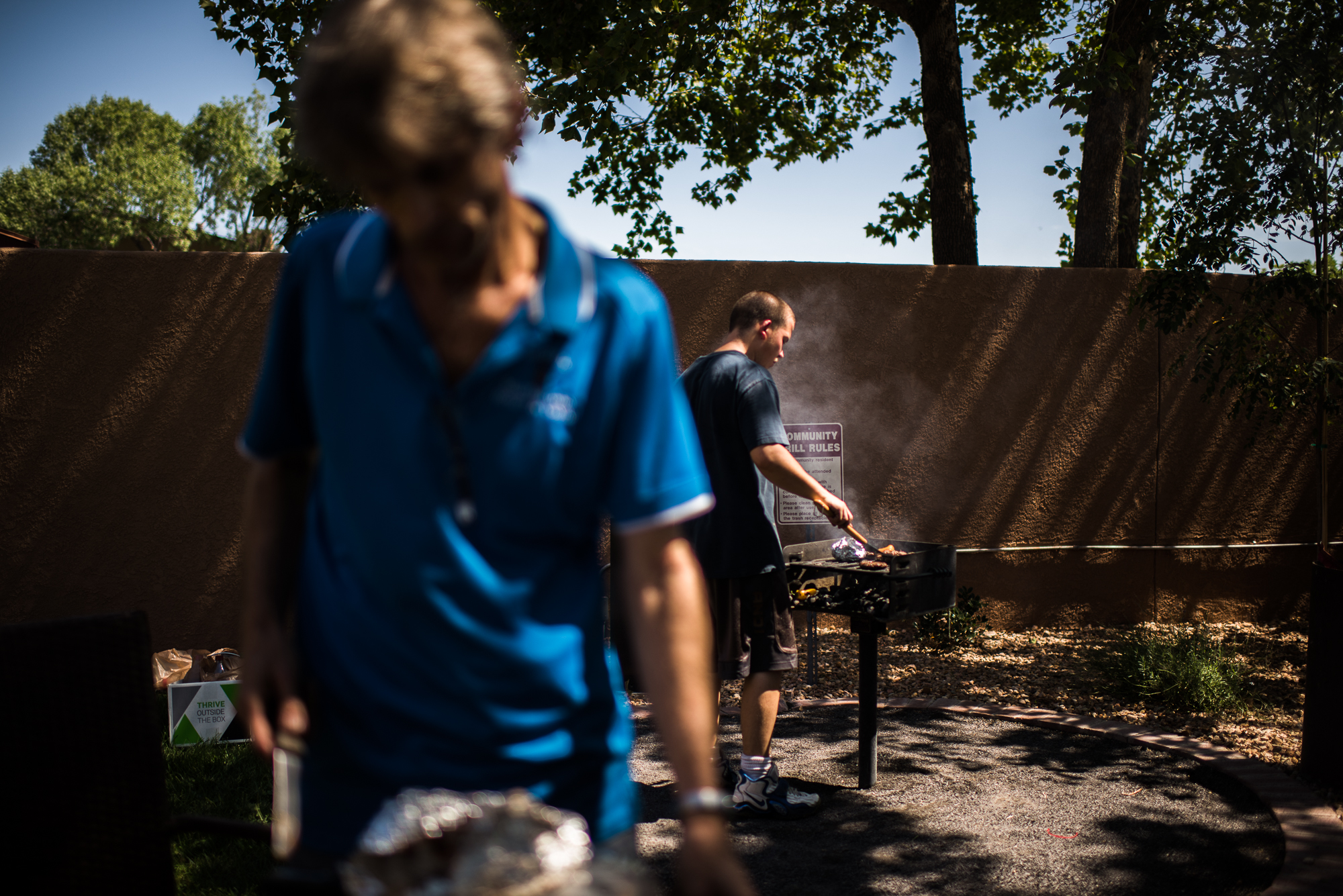 Vinny, age 18, grills meat while a family friend, Jerry, prepares the lunch table in the recreation area of the apartment complex where Jerry lives, 2017. 