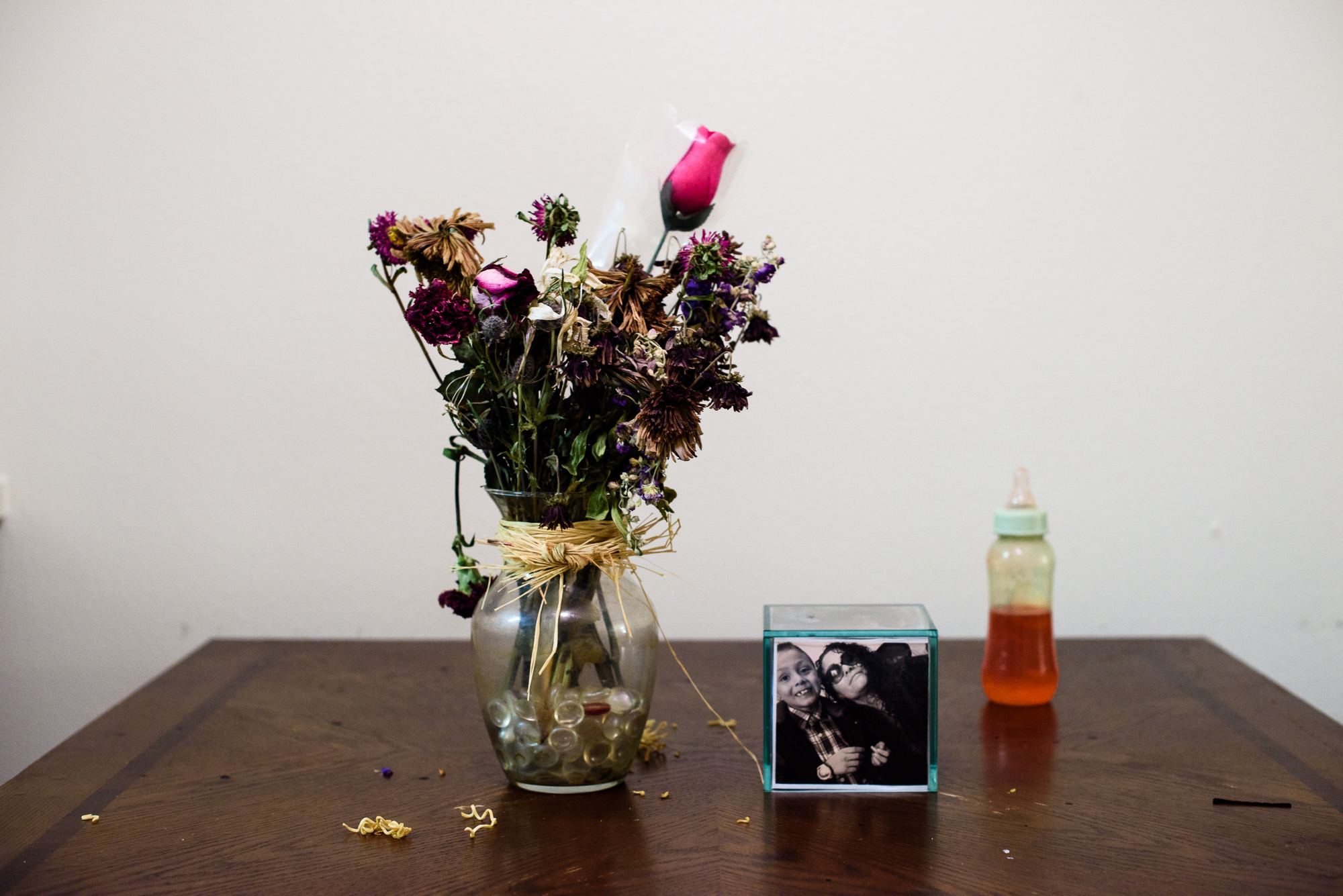  A vase of flowers, a baby bottle, and a picture of Alysia’s mom and her brother who is child protective services sits on Alysia’s dining room table. 