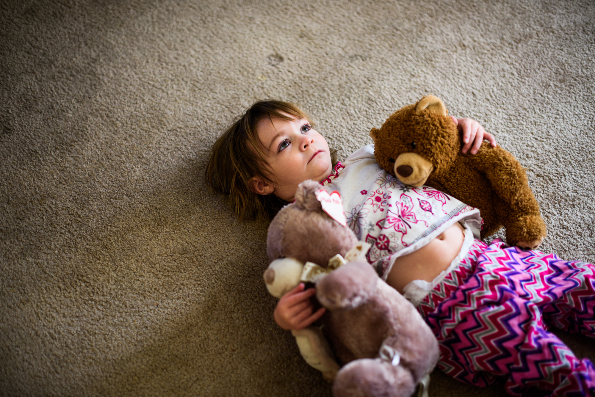  Leticia, age 2, lies on her back and holds two teddy bears.  