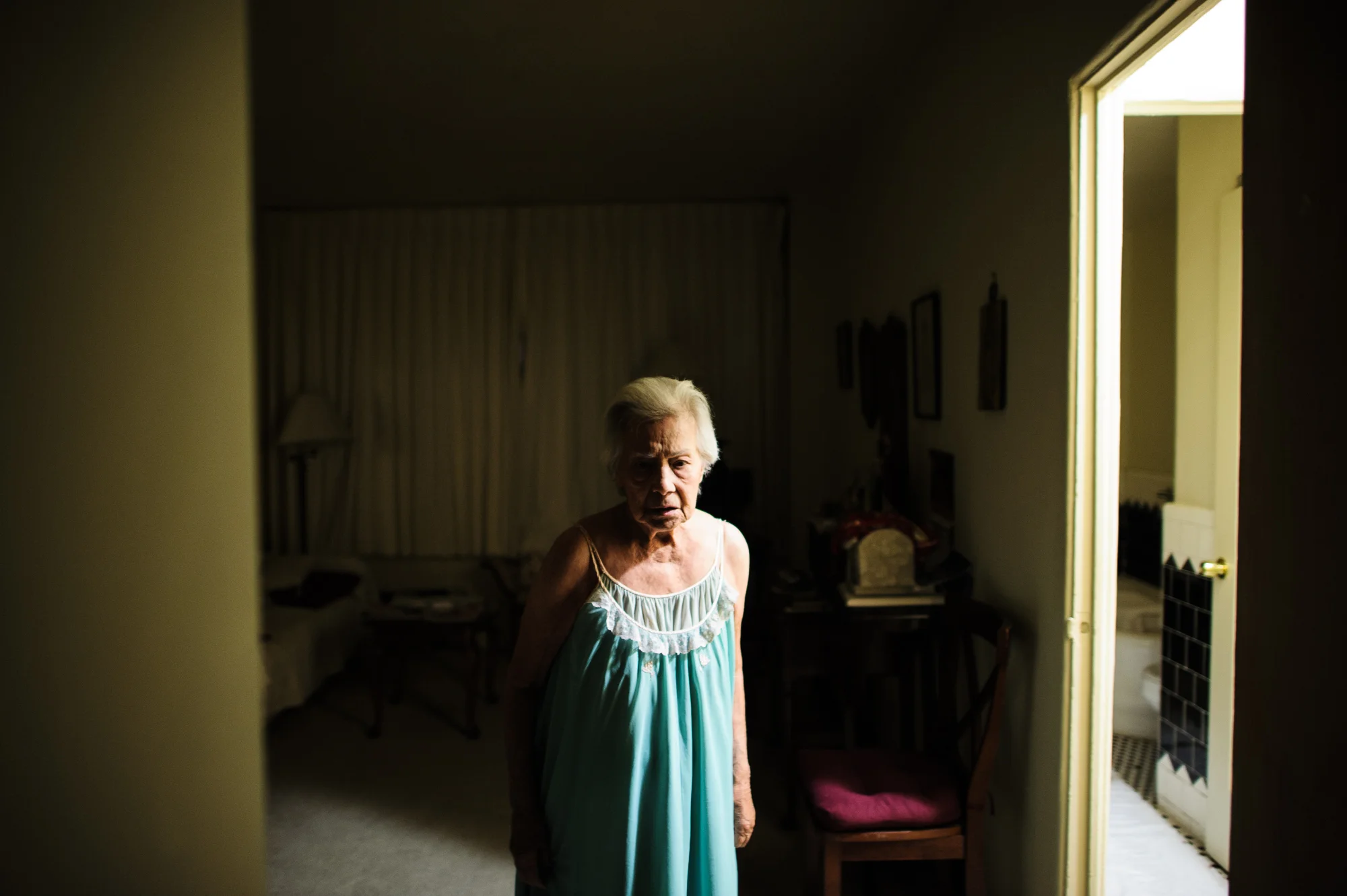 Bianca, age 86, stands her apartment at night, looking at the front door in fear that someone will come in, 2011.