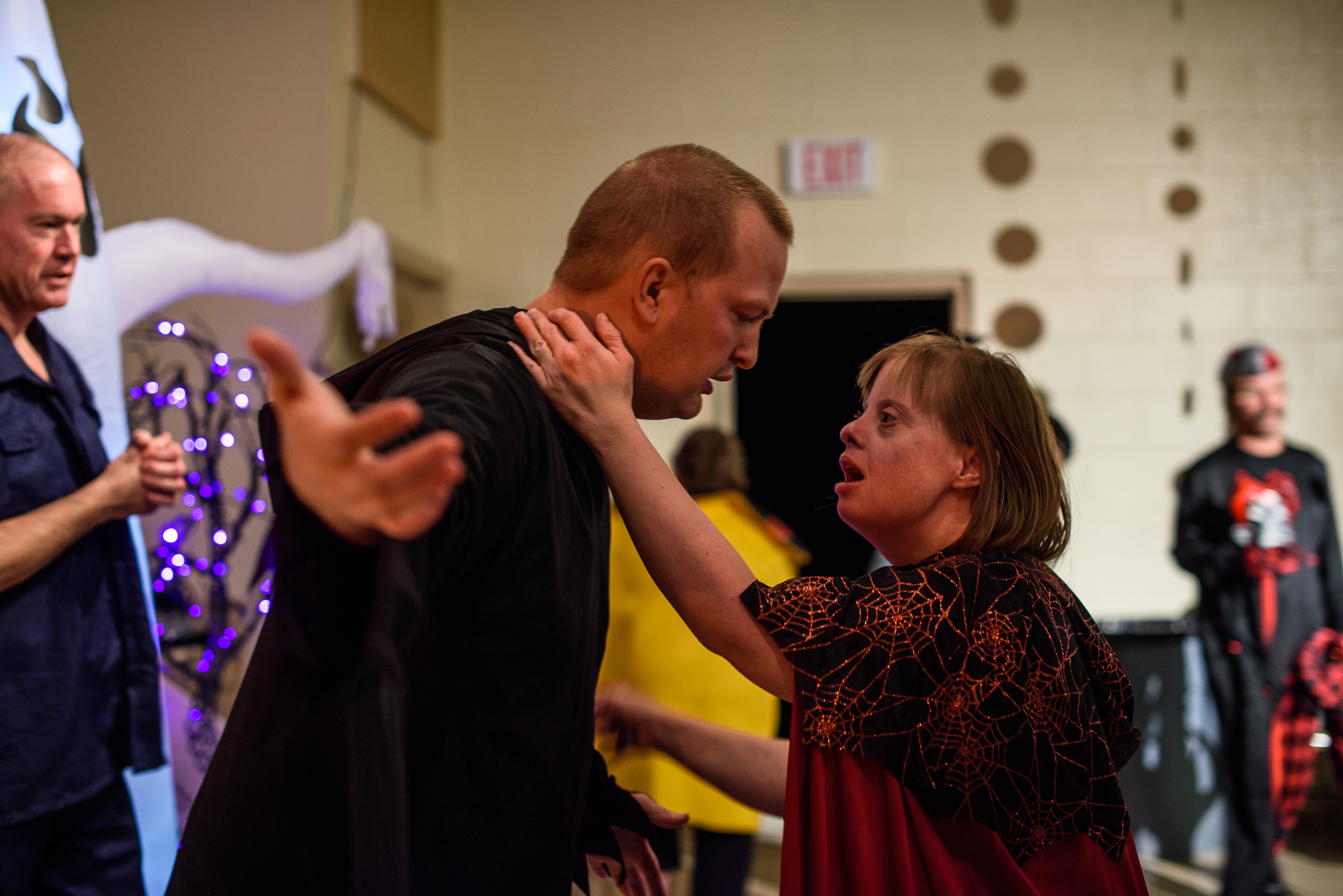 Krysta holds Nathaniel’s neck, wanting him to dance with her at the Halloween party; Krysta is upset that Nathaniel is ignoring her and is spending his time with other men.