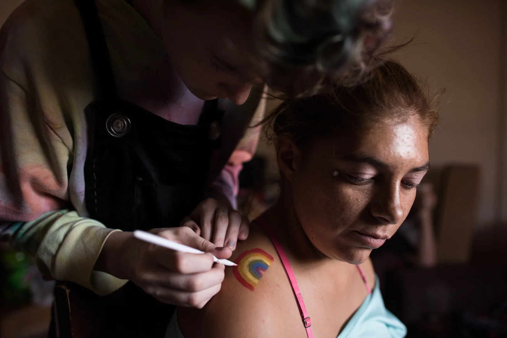 Adrian, age 16, paints a rainbow on Delilah’s shoulder; Adrian is Alex’s younger brother. Adrian transitioned from female to male four years ago.