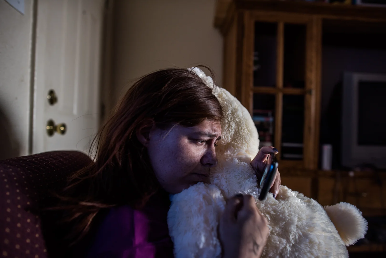 Delilah holds a bear as she watches a music video after finding out how her father brutally died; Delilah reconnected with family she has never met through Facebook after fleeing Albuquerque.
