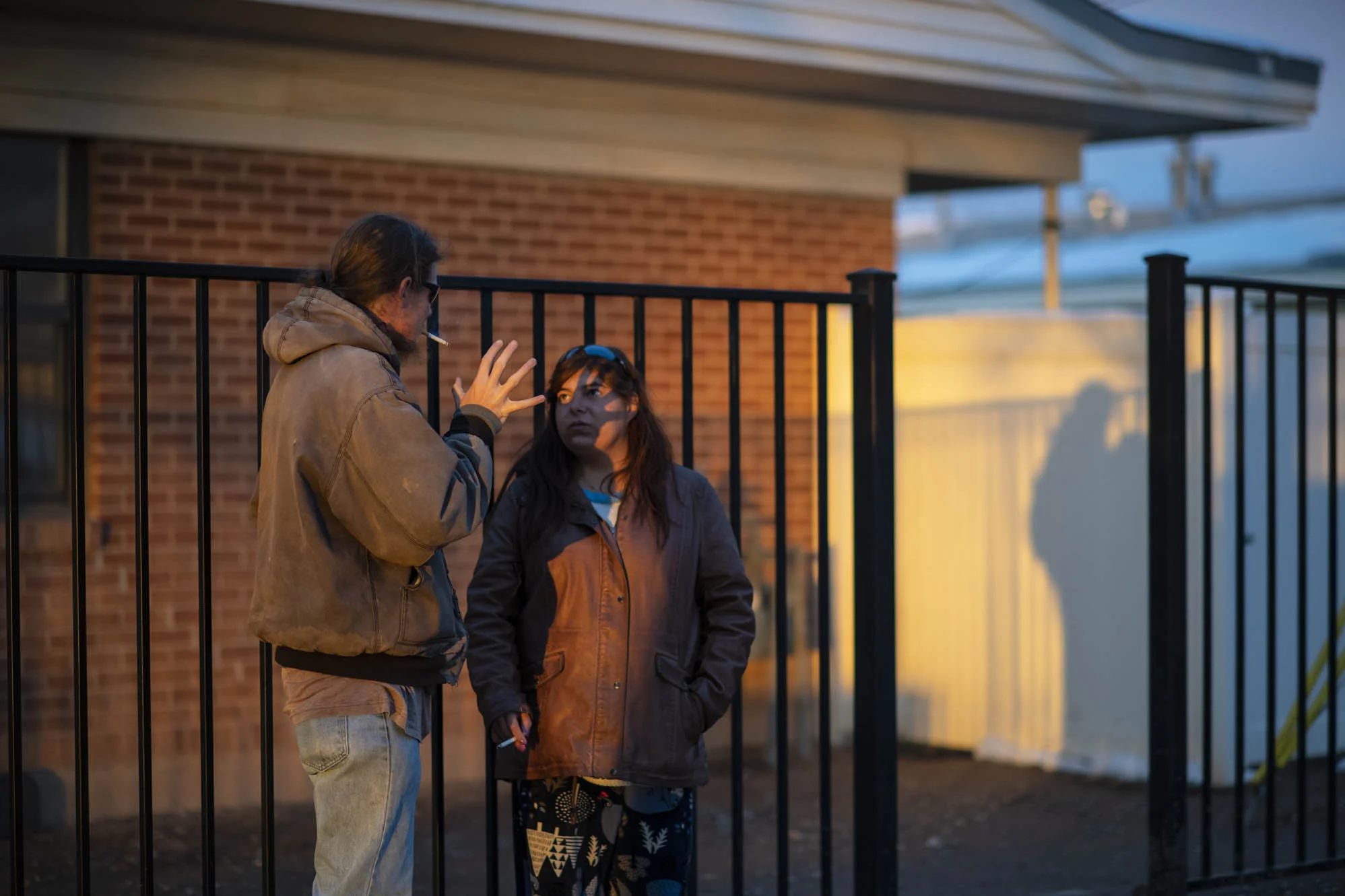 Alex and Delilah smoke and stand in the alley next to the apartment where they live.