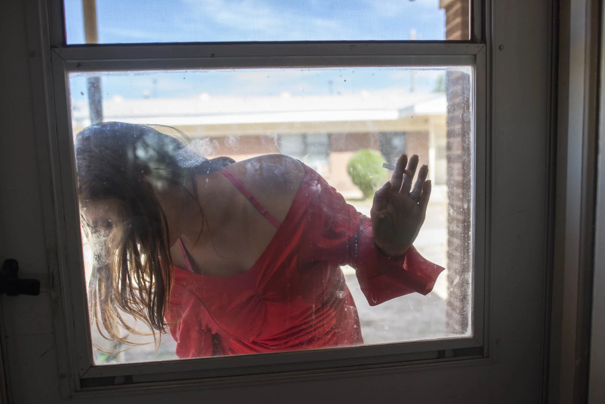 Delilah places her hand on the window, as she fixes her heel on the porch.