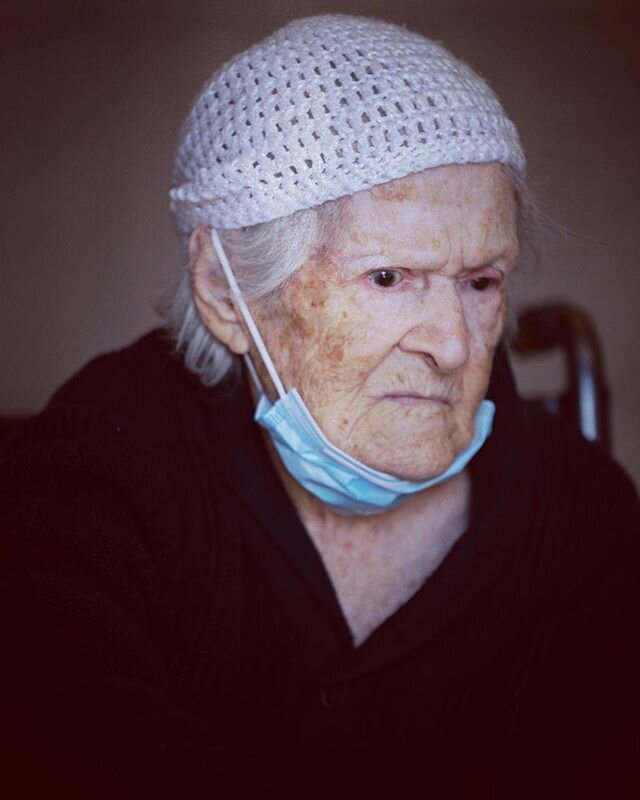 Olivia, age 102, sits in her wheelchair in the lobby, as she listens to her daughter, Maria, who stands in the doorway at the Alexandria Care Center on May 10. #mother @nytimes