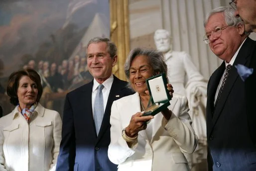 Rachel Robinson (holding award) accepts the posthumous Congressional Gold Medal for her husband from President George W. Bush in a March 2, 2005, ceremony in the Capitol Rotunda. Also pictured are Nancy Pelosi and Dennis Hastert. Photo via the White House.