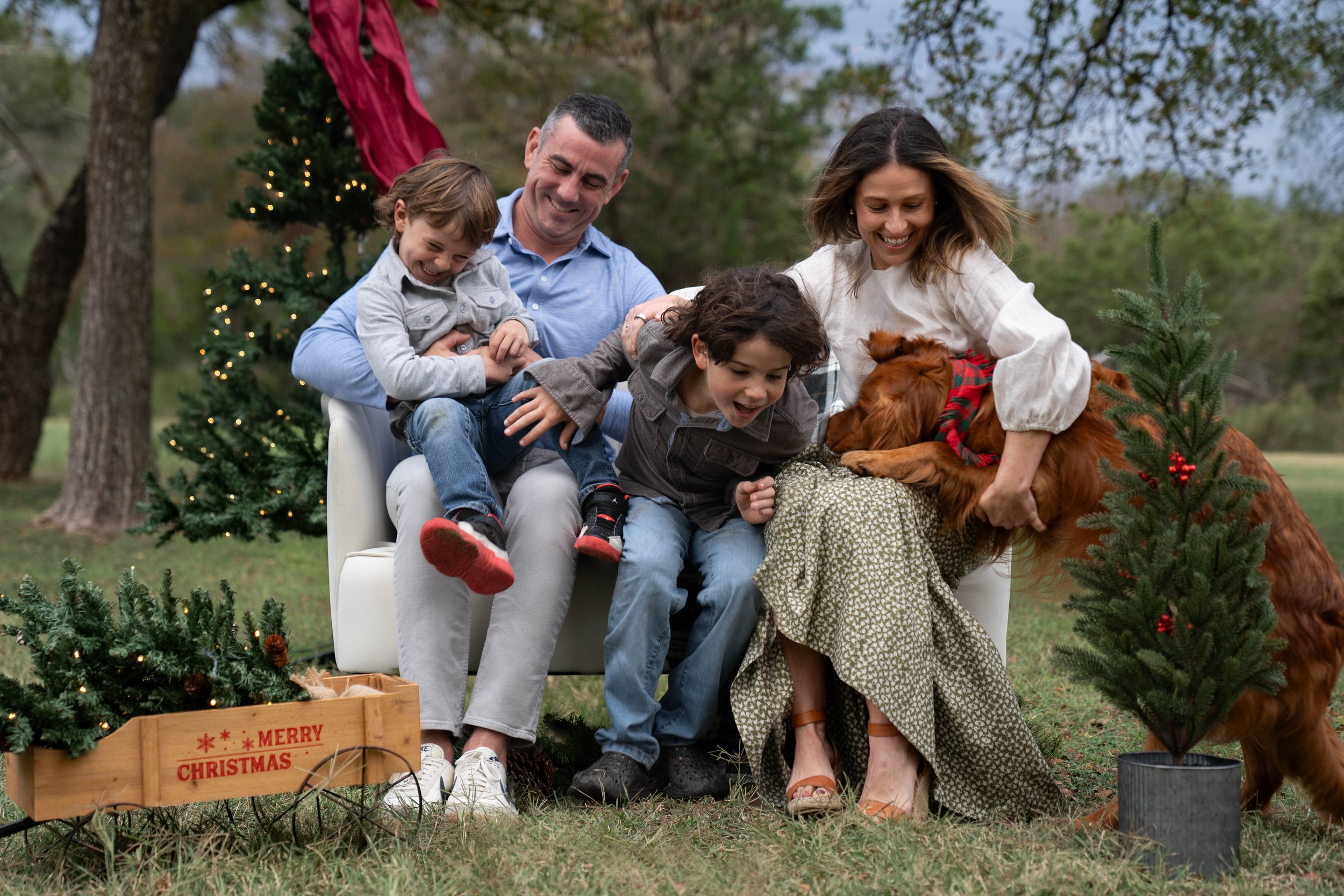 Family laughing on a white sofa in front of a Christmas tree during a Christmas mini session in Austin