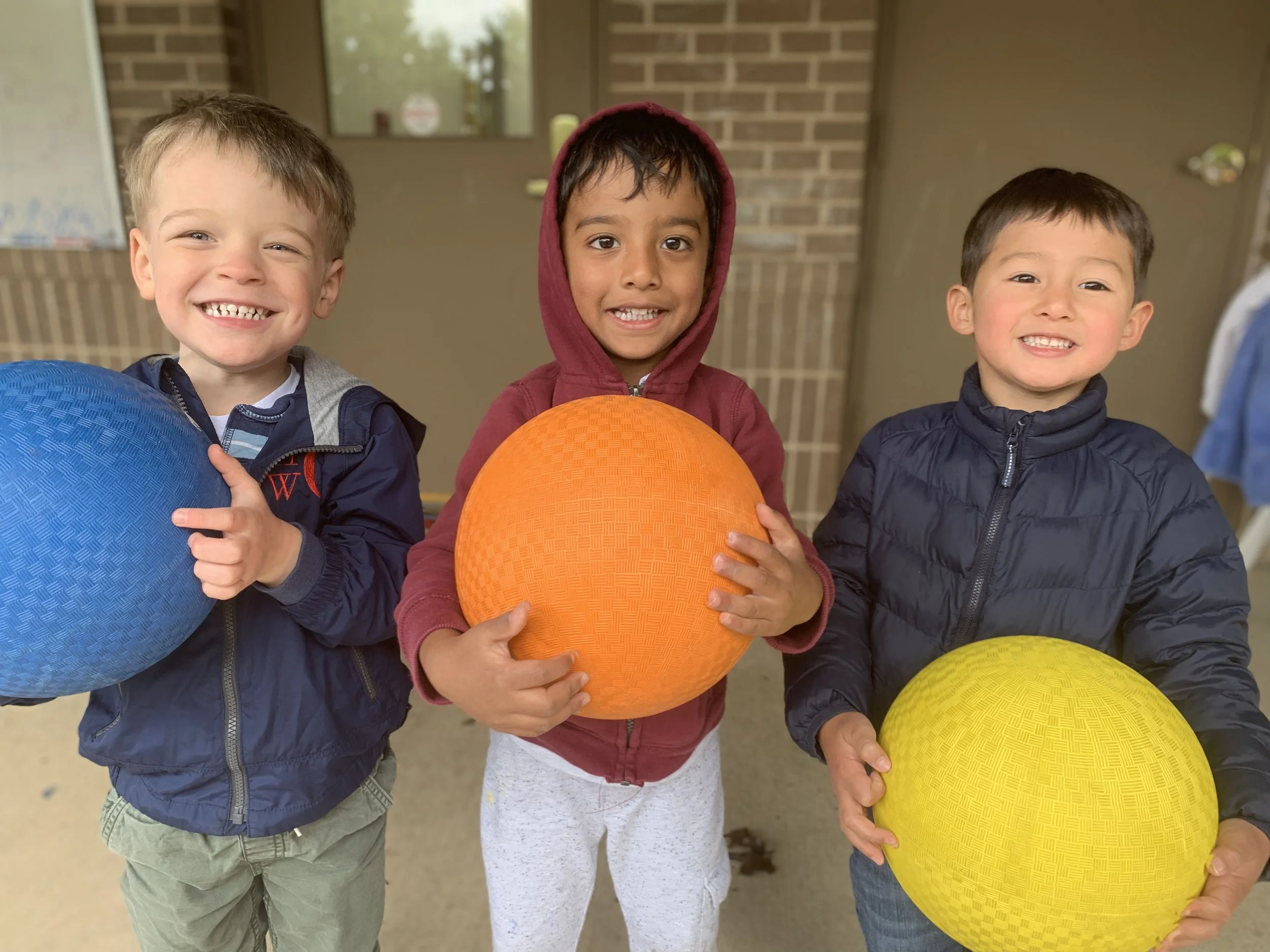 Three children holding playground balls outside