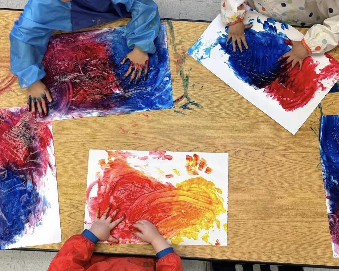 Children are wearing smocks and finger painting using primary colors