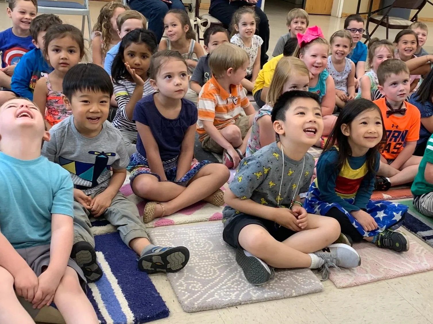 Children sitting on carpet squares laughing and smiling while watching a presentation