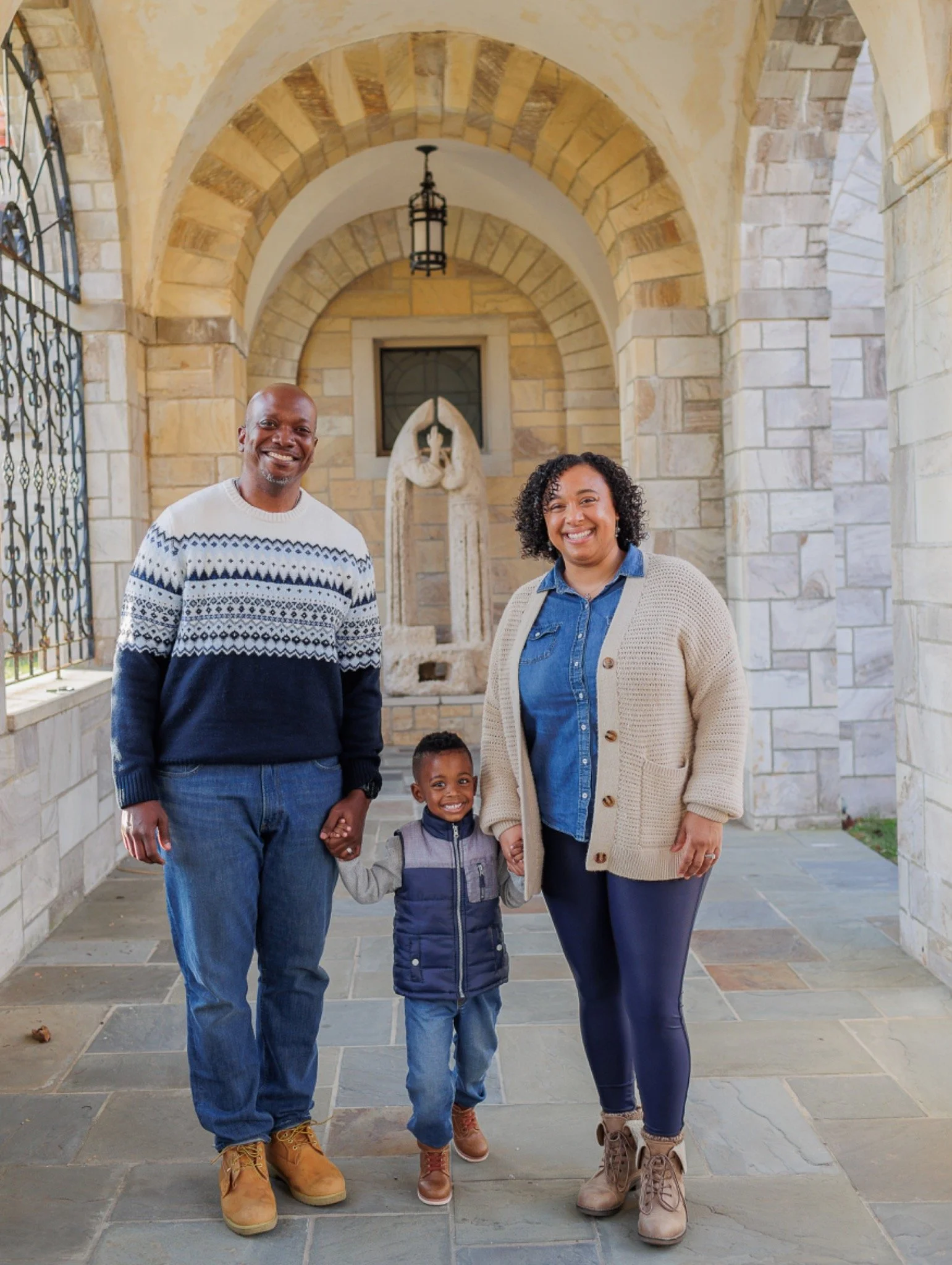 Family of three holding hands under stone arch at the Shrine of St. Anthony in Clarksville, Maryland.