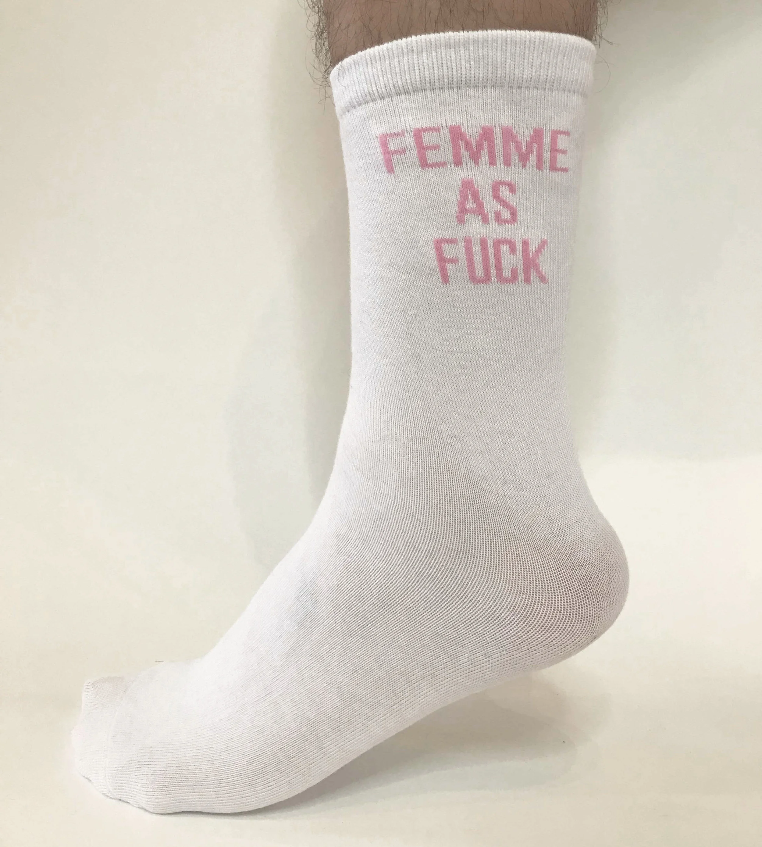 Image of foot wearing a white, calf high sock with pink text, “femme as fuck”