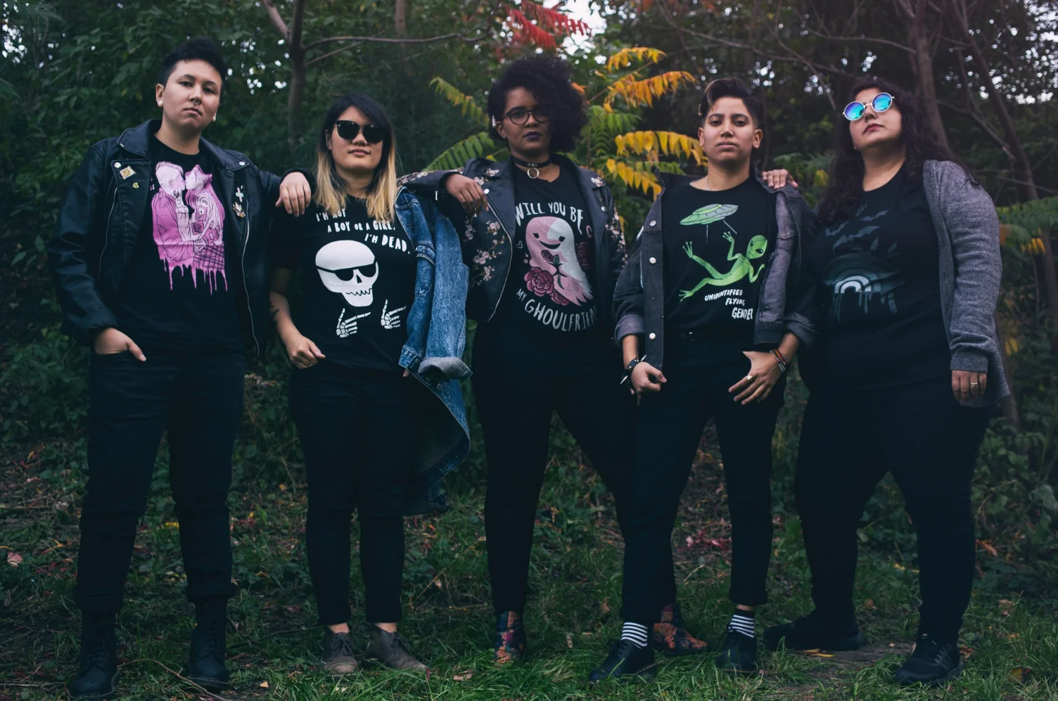 Image of five people lined up in a forest, all wearing jackets over various graphic ghost and alien prints on t-shirts