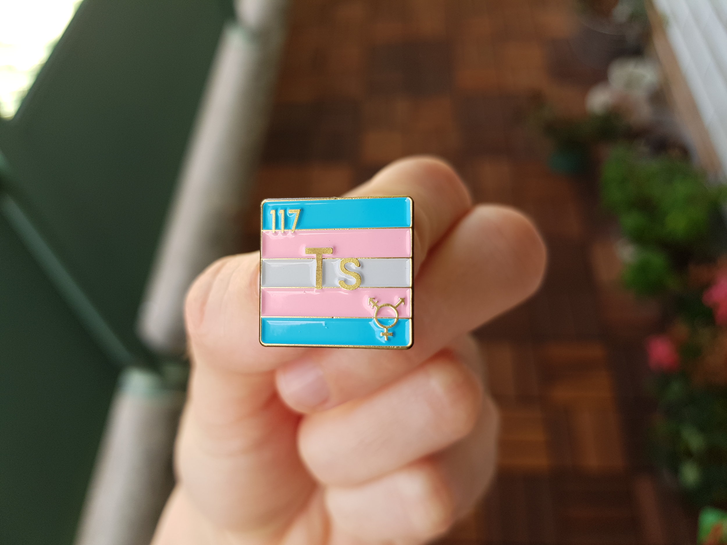 Image of hand holding a periodic element pin with the transgender pride flag