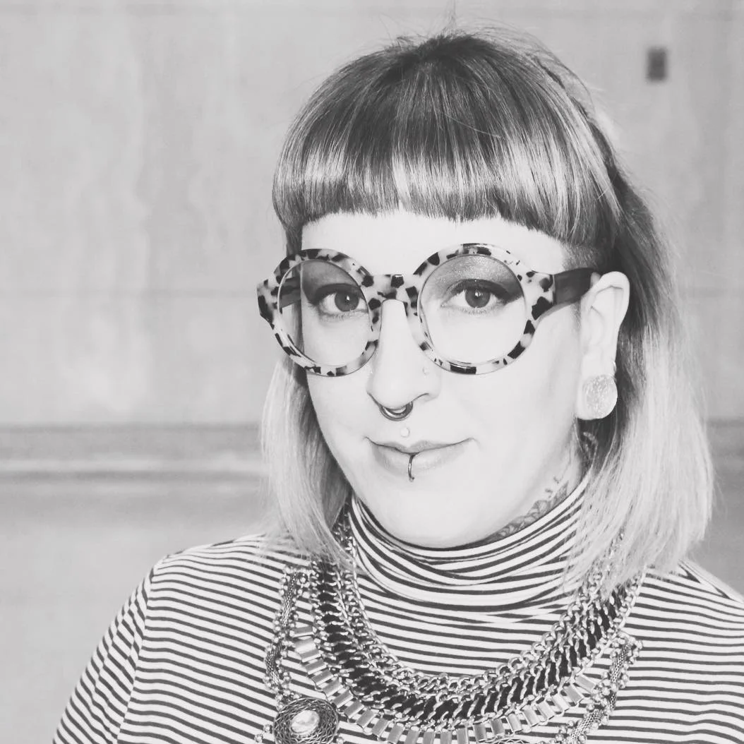 Close up greyscale image of Alysia wearing glasses and smiling at the camera