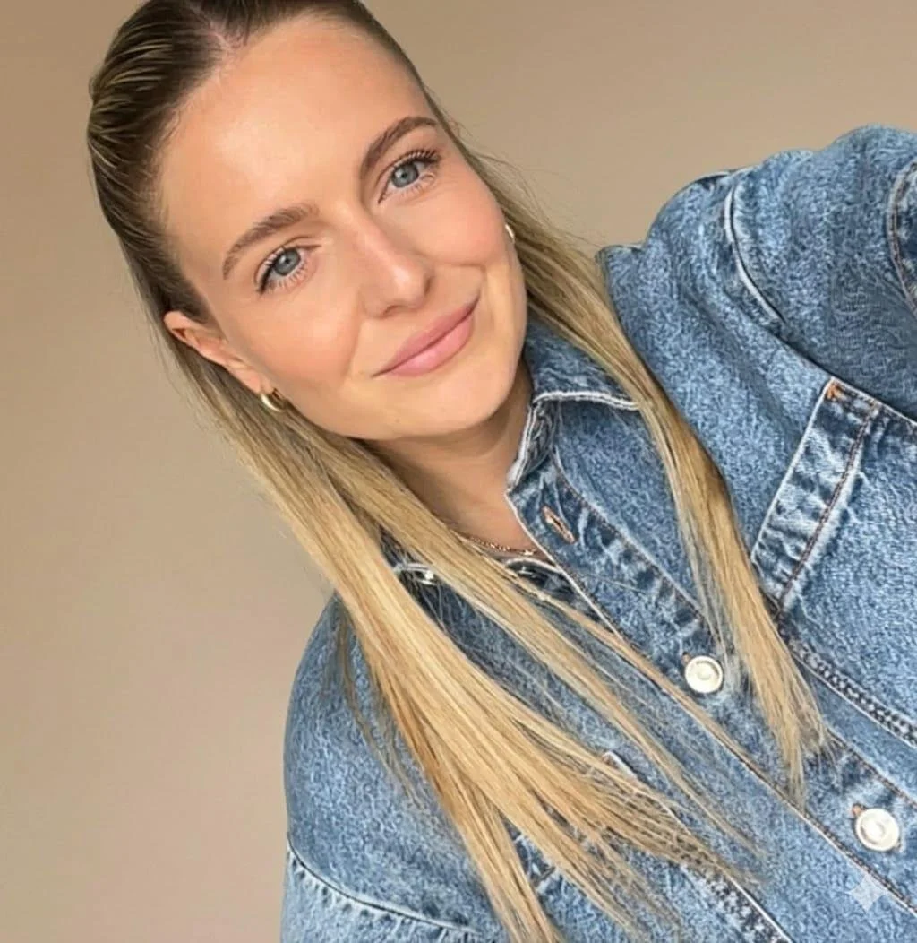 Junge Frau mit blonden Haaren, blauen Augen, lächelt, trägt eine Jeansjacke, Hintergrund beige