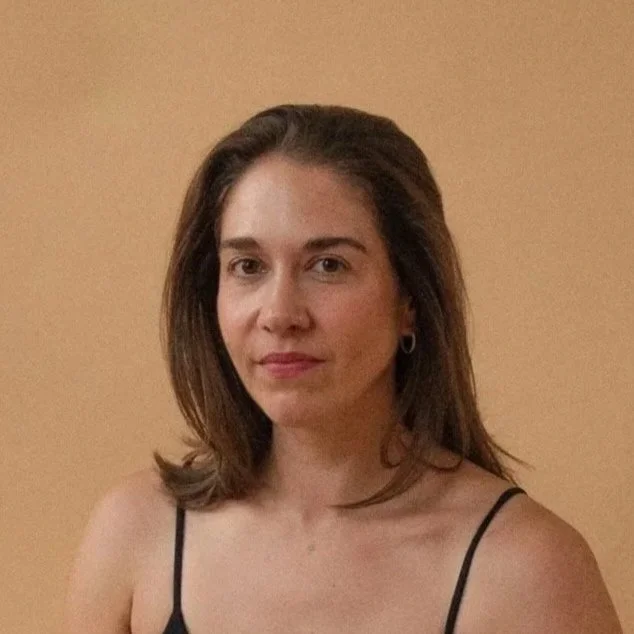 Ein junges Mädchen mit braunen Haaren, das in die Kamera blickt, auf einem beige Hintergrund.