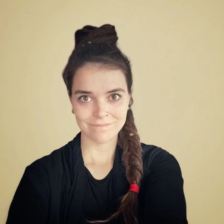 Junge Frau mit dunklen Haaren, gefeilten Haaren, in einem schwarzen Oberteil, vor einem hellen Hintergrund.