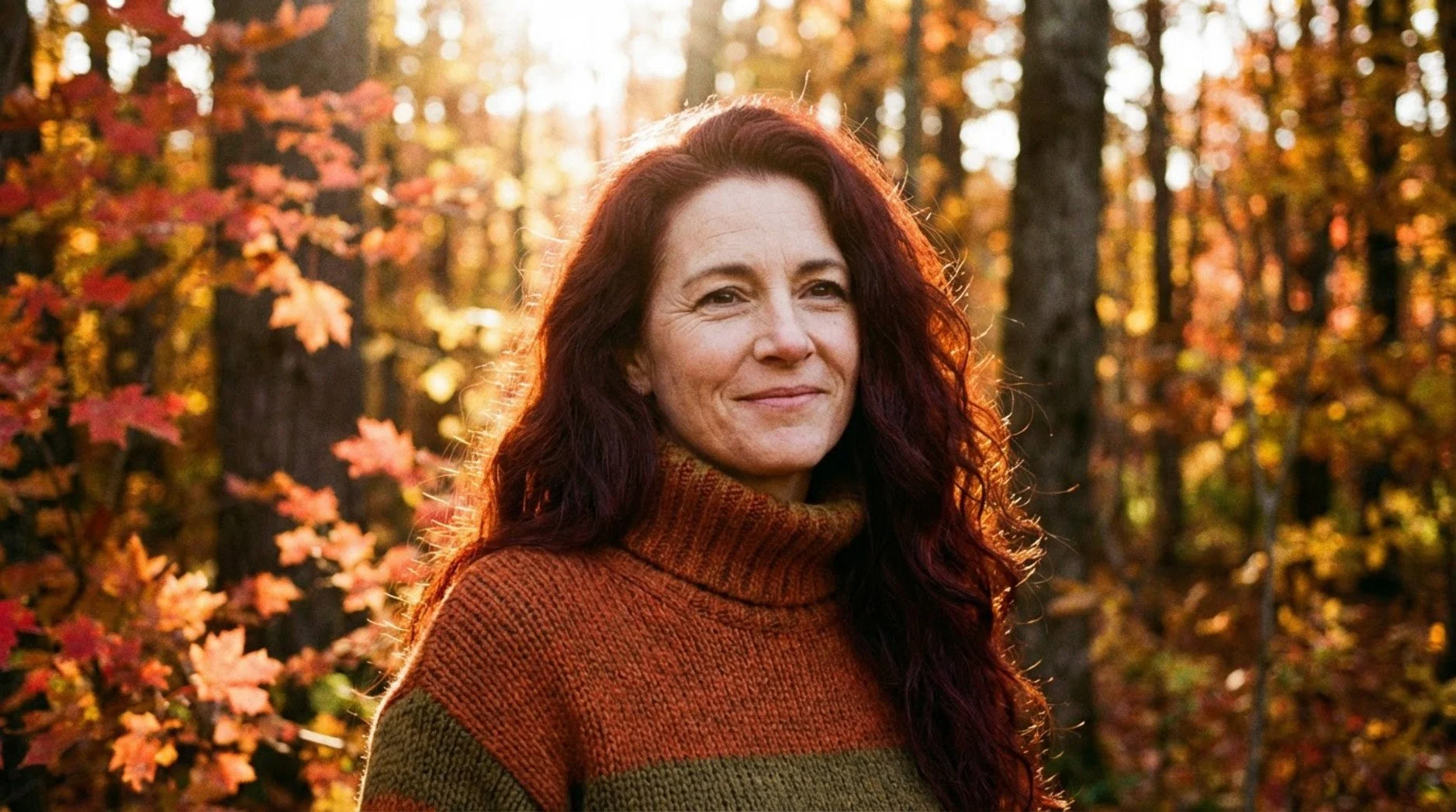 A stylish portrait of a woman with vibrant auburn hair in an autumn setting with warm light filtering through trees.