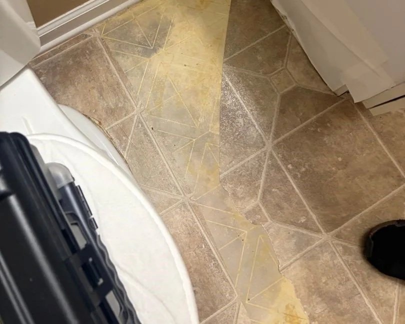 Photo shows 2 layers of vinyl flooring in bathroom after part of the top layer was removed by ServiceMaster during a water damage mitigation