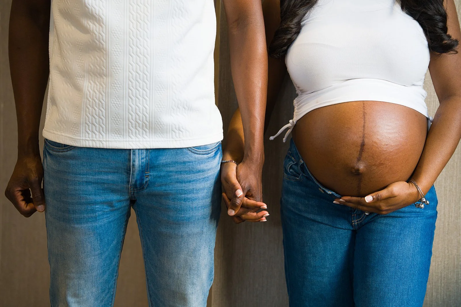 A couple holds hands in jeans in a white shirt in Ithaca New York as they prepare to welcome their new baby