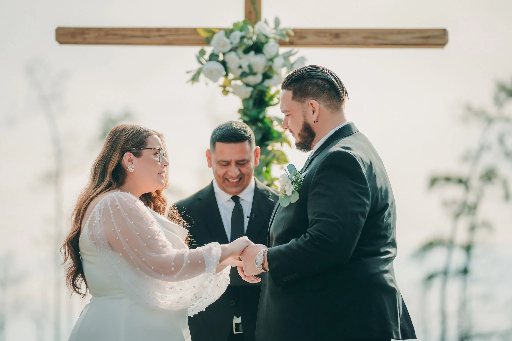 bride and groom standing up with pastor and a cross in the background