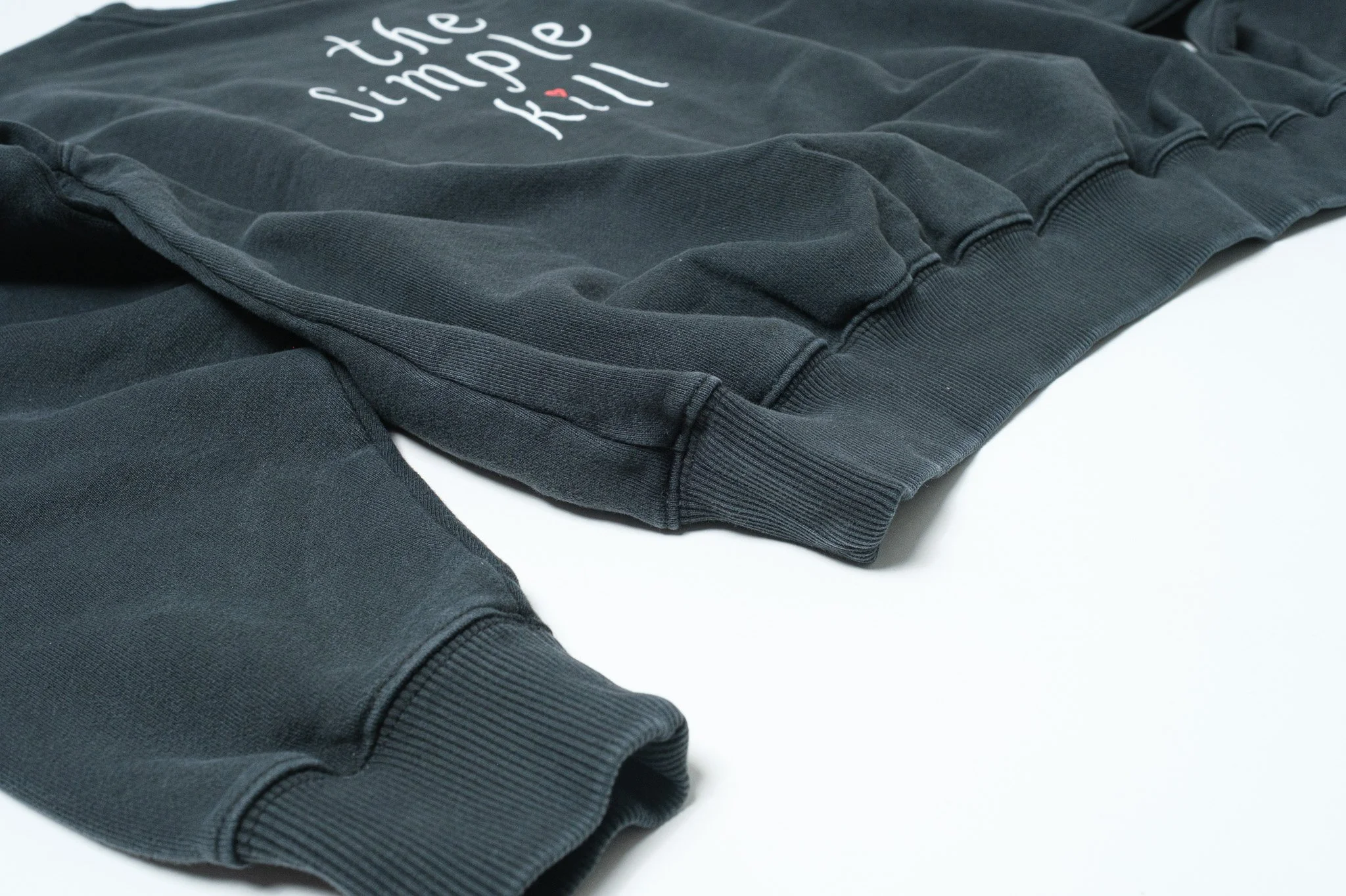 Close-up of a black sweatshirt with the words 'the simple' written on it in white letters and a red heart above the 'i'.