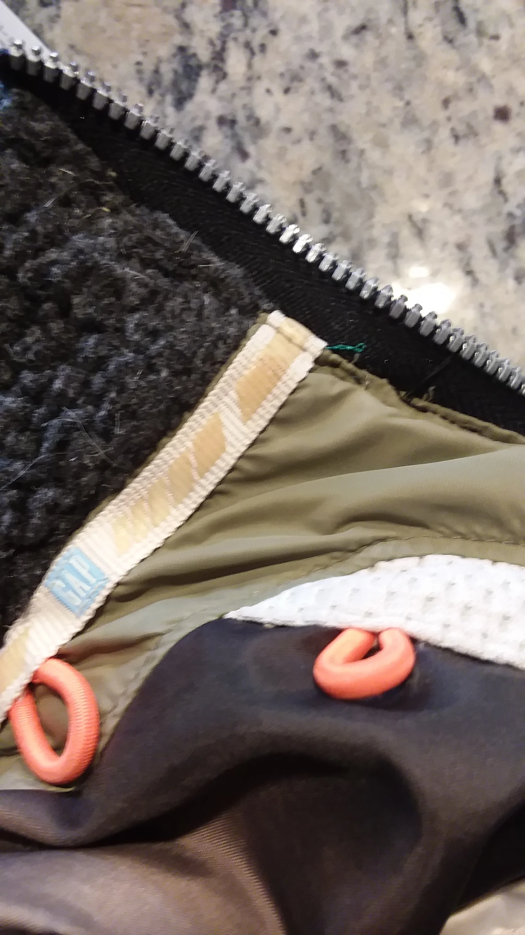 The white trim you see with the word GAP on it did NOT want to be sewn through. So I skipped that portion with my sewing machine (black thread) and went back and sewed the zipper in by hand for about an inch around the thick trim. You can see a bit of green thread which is what I used to sew by hand.