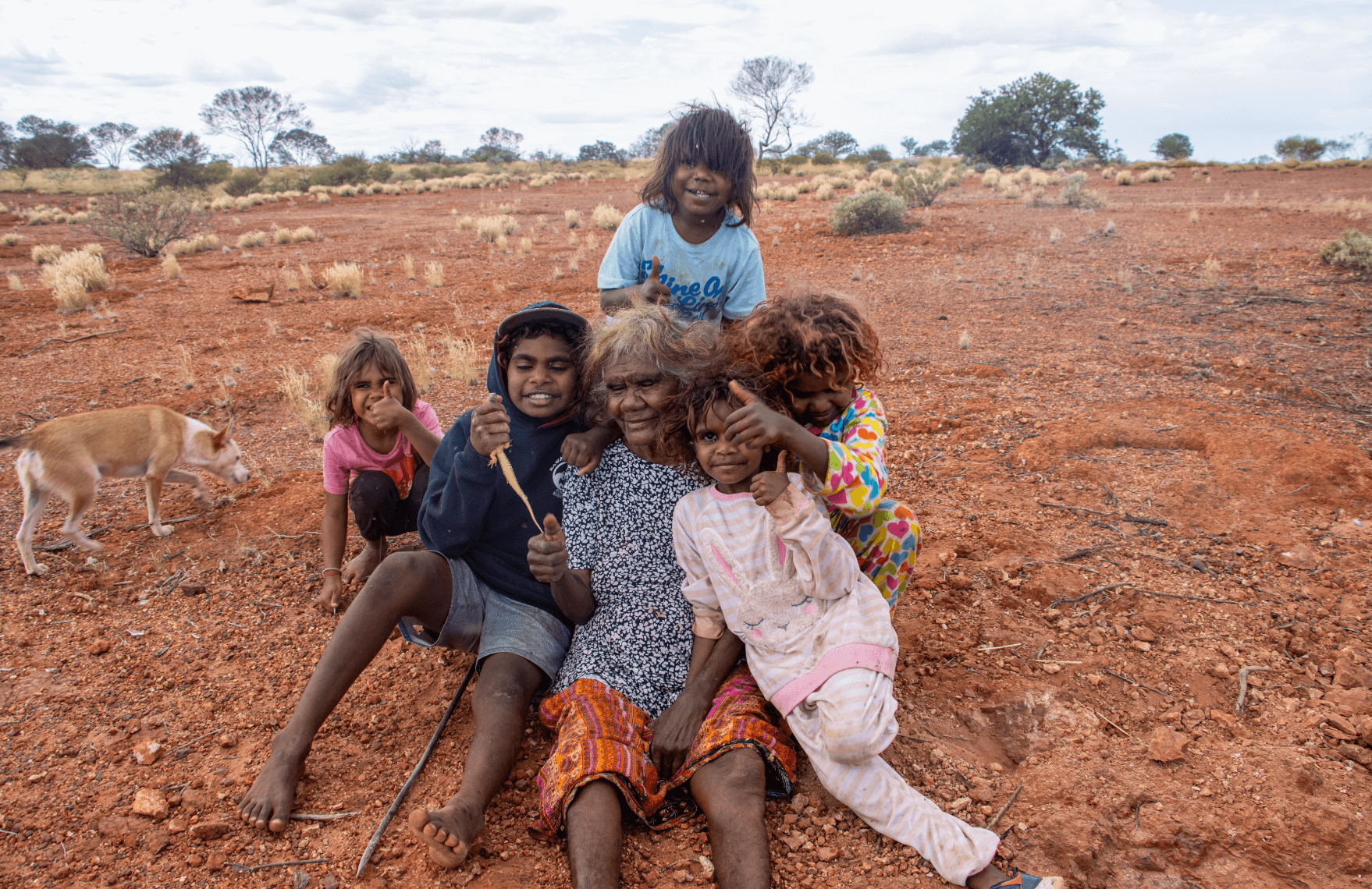 Martu Elder and children sitting together on-Country, reflecting the Martu Outcomes and a shared vision for a strong future shaped by Martu and supported by Kanyirninpa Jukurrpa.